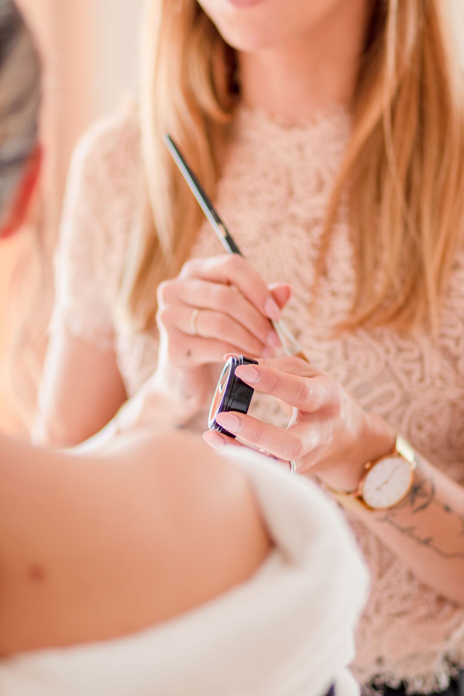 Person wearing lace top holding makeup brush and cosmetics during bridal preparations.
