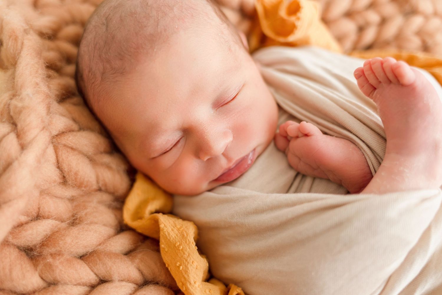 Closeup newborn photography featuring soft peach tones and knitted textures.