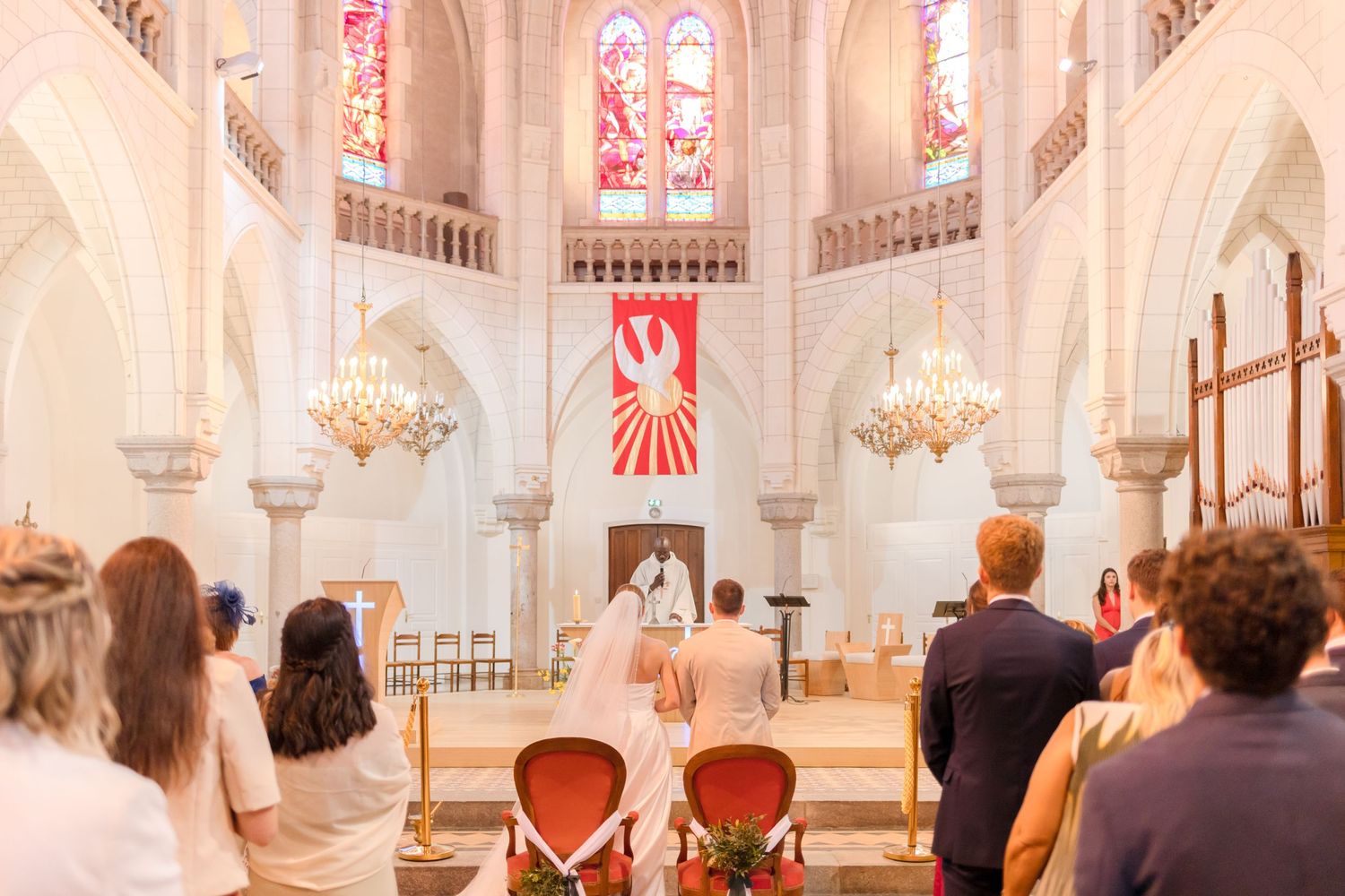 A wide view of a Catholic church wedding ceremony with guests seated in wooden pews.