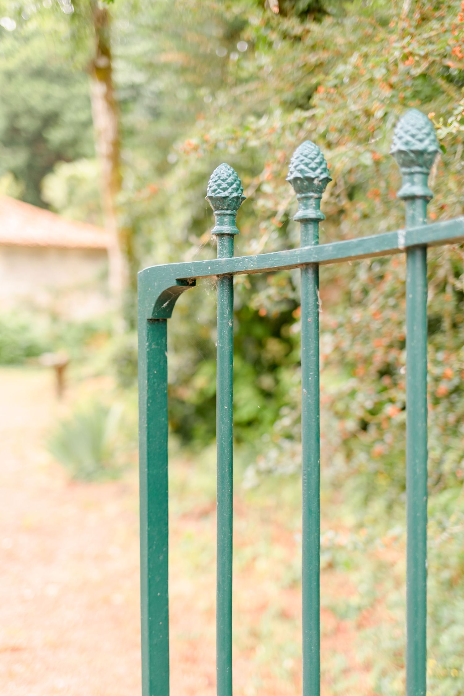 Decorative green metal fence posts with pine cone finials against blurred foliage.