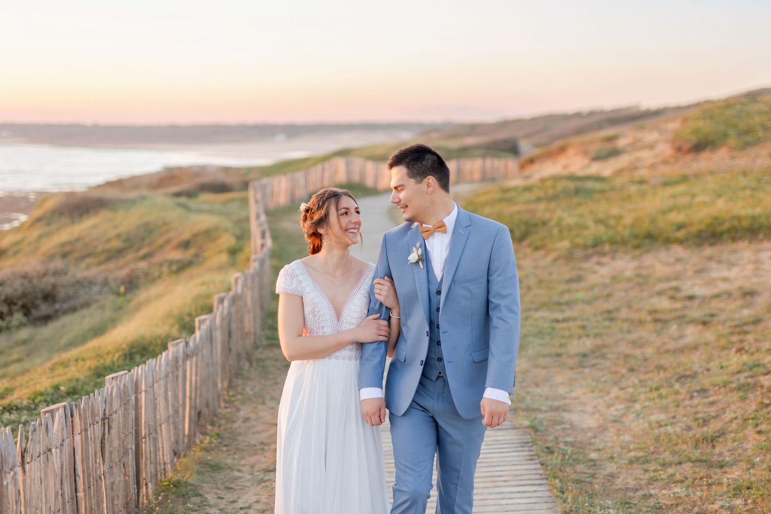 Romantic wedding photo of couple walking along coastal path at dusk.