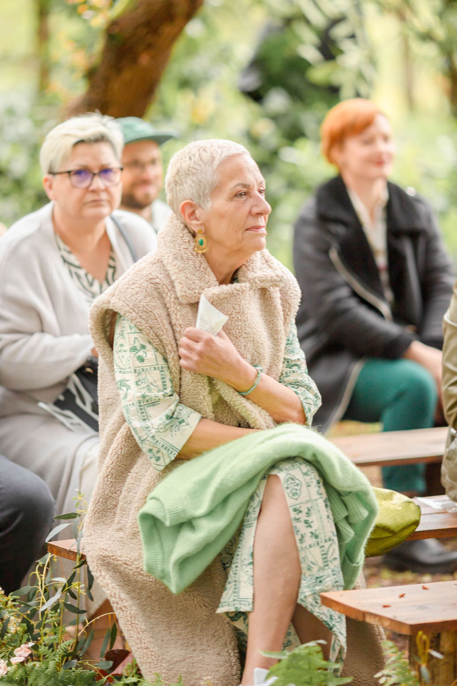 Guests in cozy attire seated on wooden benches during an outdoor event.