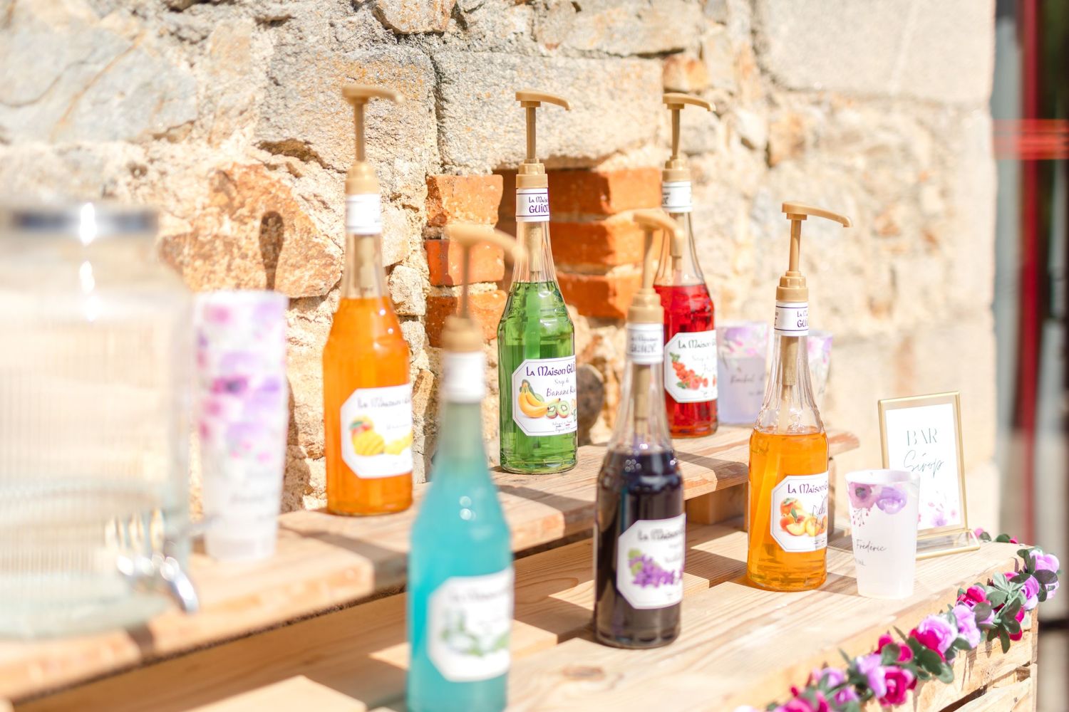Colorful bottles of drinks arranged on a rustic stone bar counter with floral decorations.