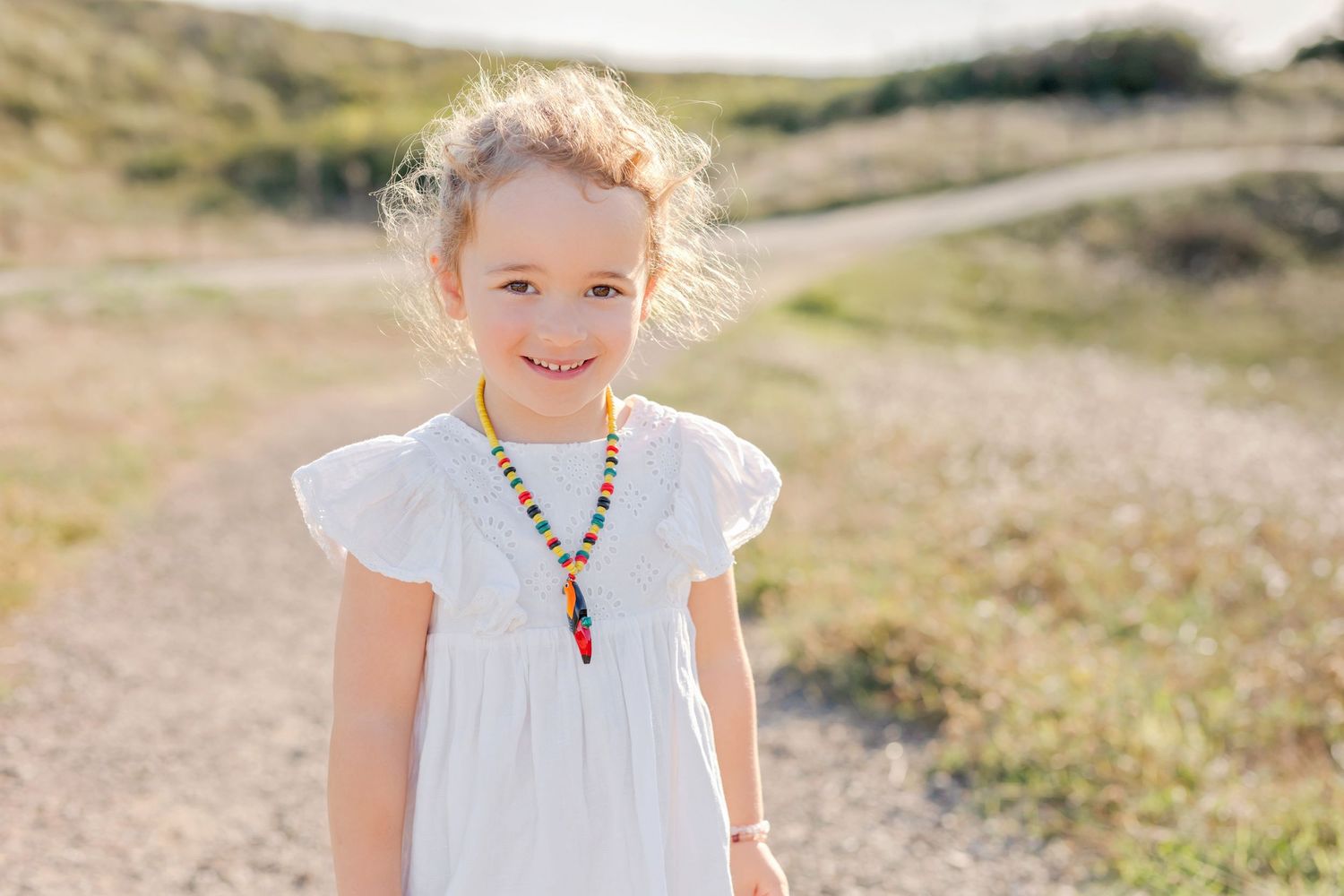 Close up portrait of child wearing white dress and colorful beaded necklace outdoors.