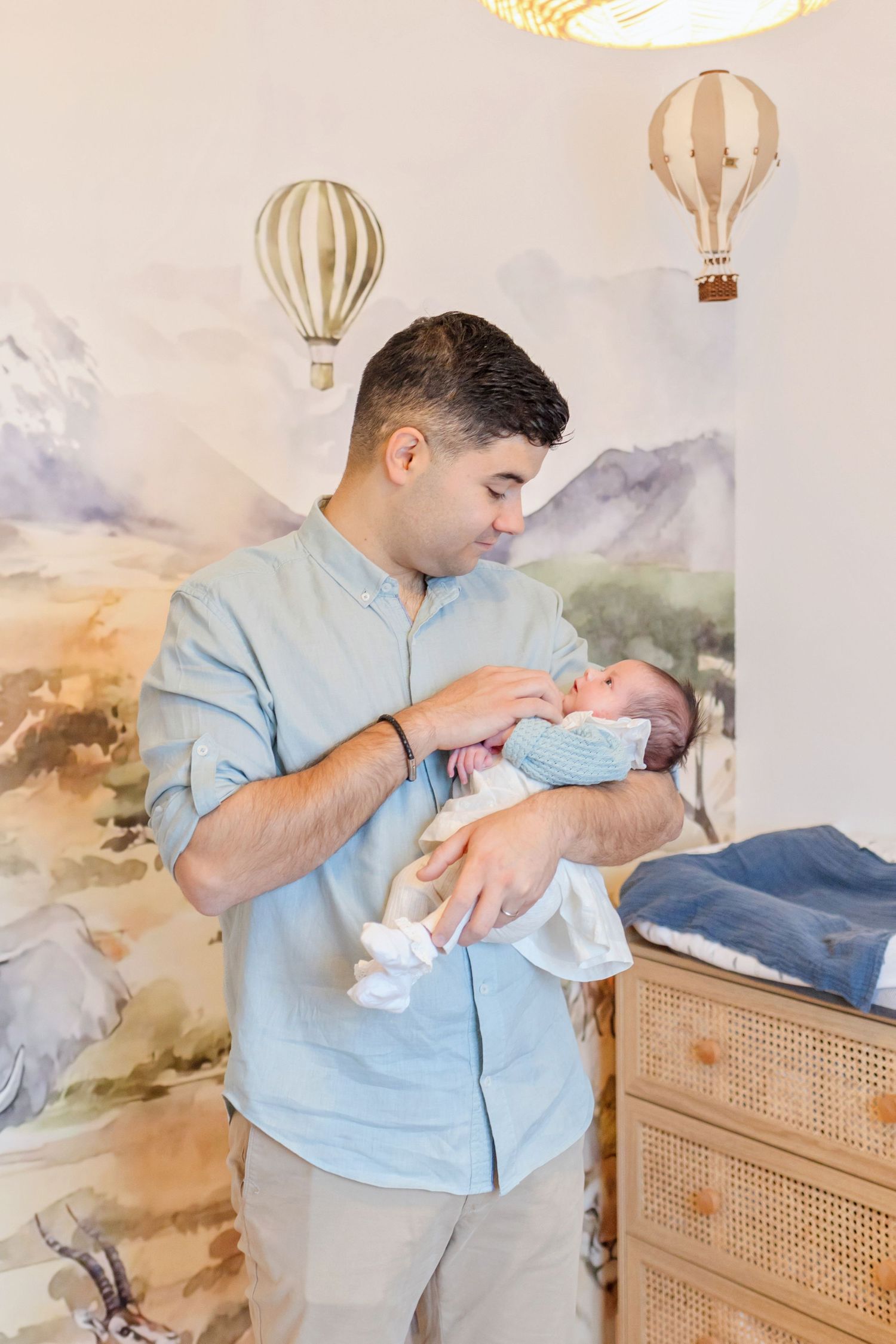 Nursery with hot air balloon decor and mountain mural while attending to infant.