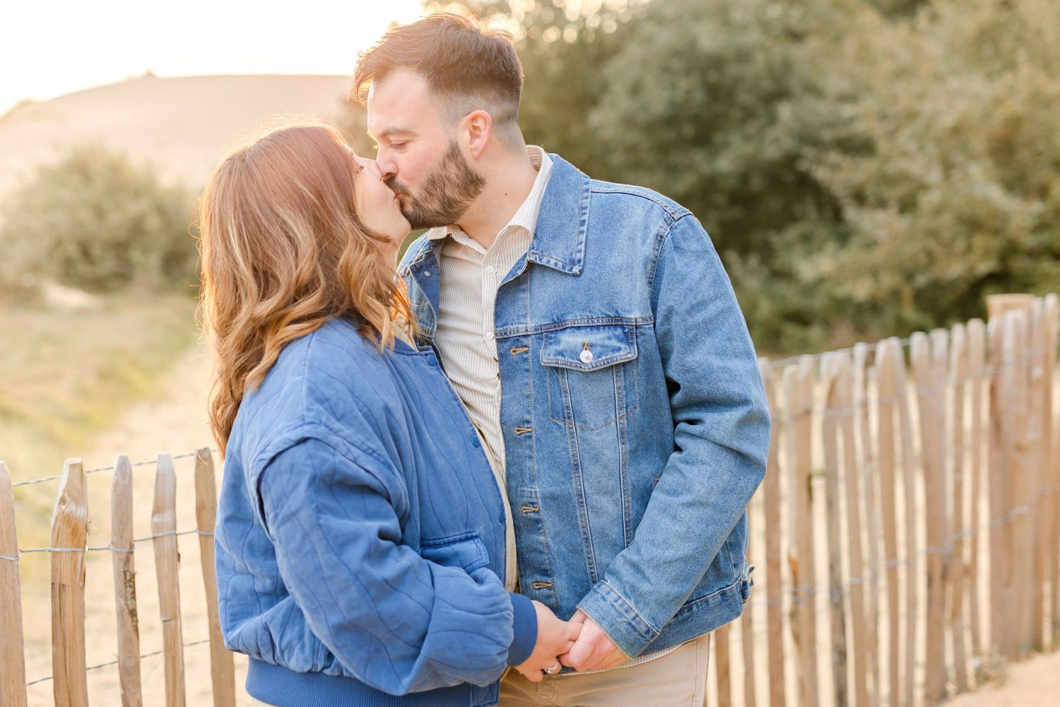 Couple in denim sharing romantic moment by rustic fence at sunset.