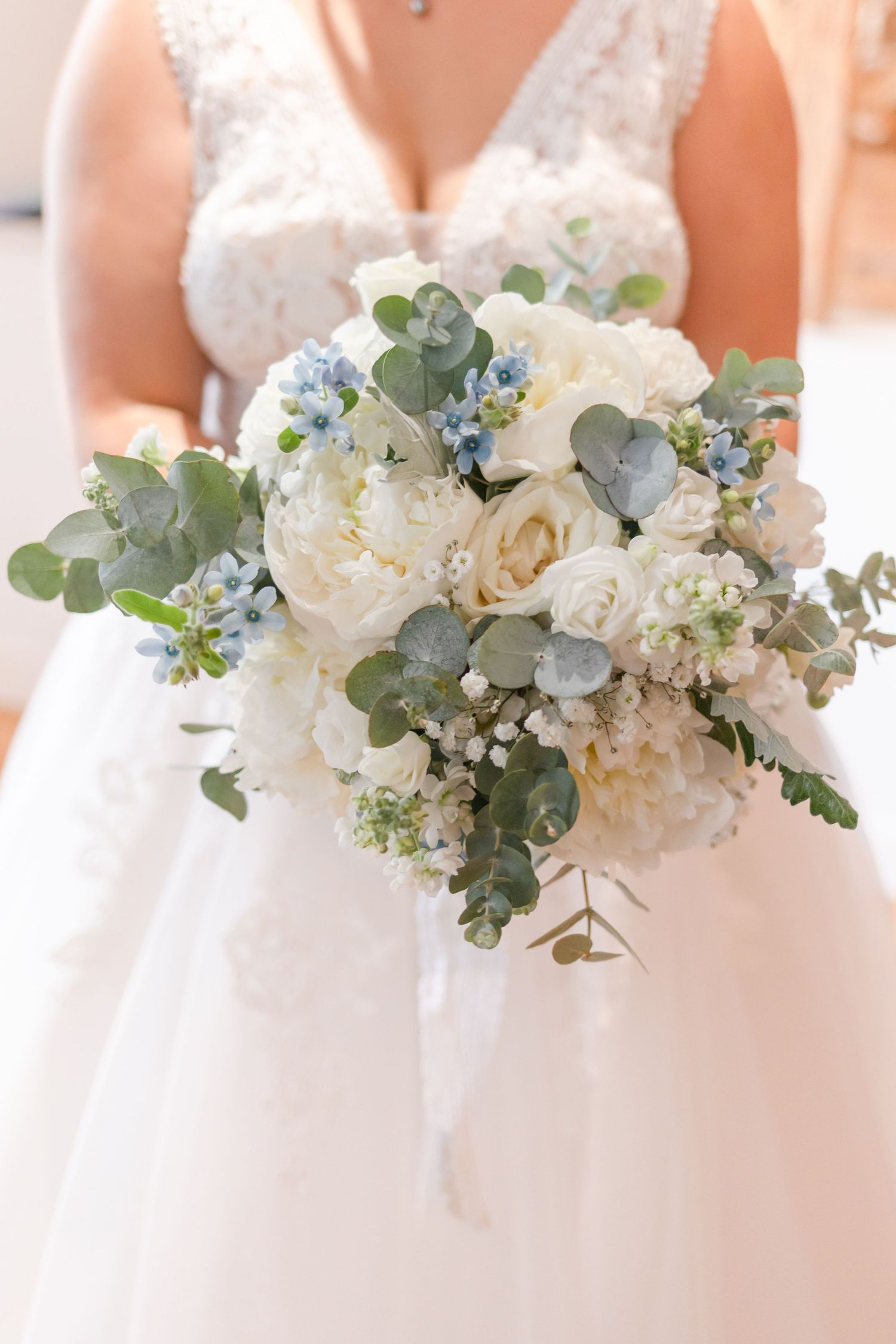 An elegant white and blue wedding bouquet with peonies, roses, and eucalyptus leaves.