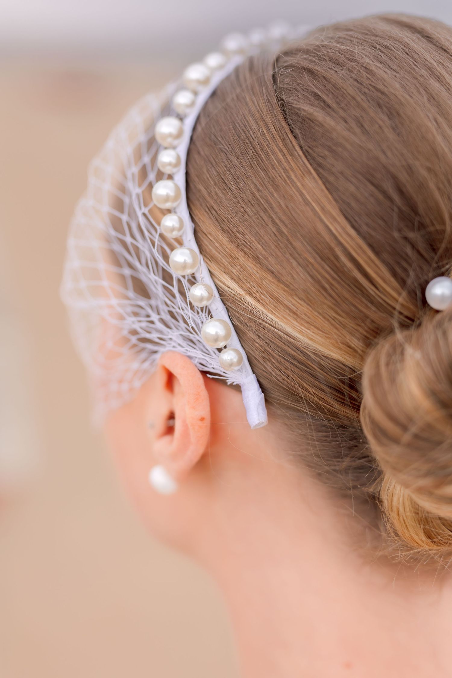 Close-up detail of delicate pearl and lace bridal headpiece against blonde hair.