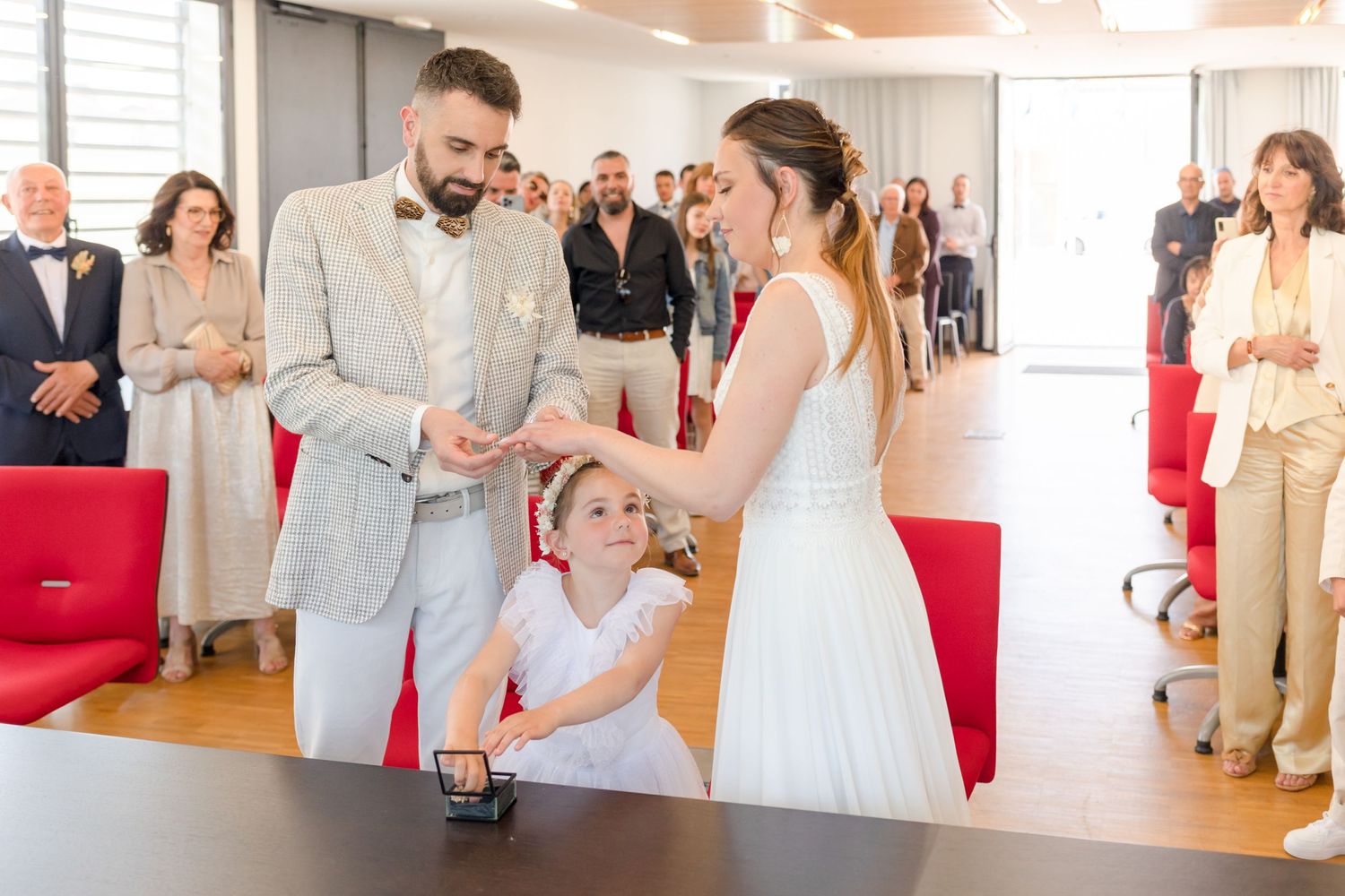 Guests watch an emotional wedding ceremony in a bright venue with red seating.