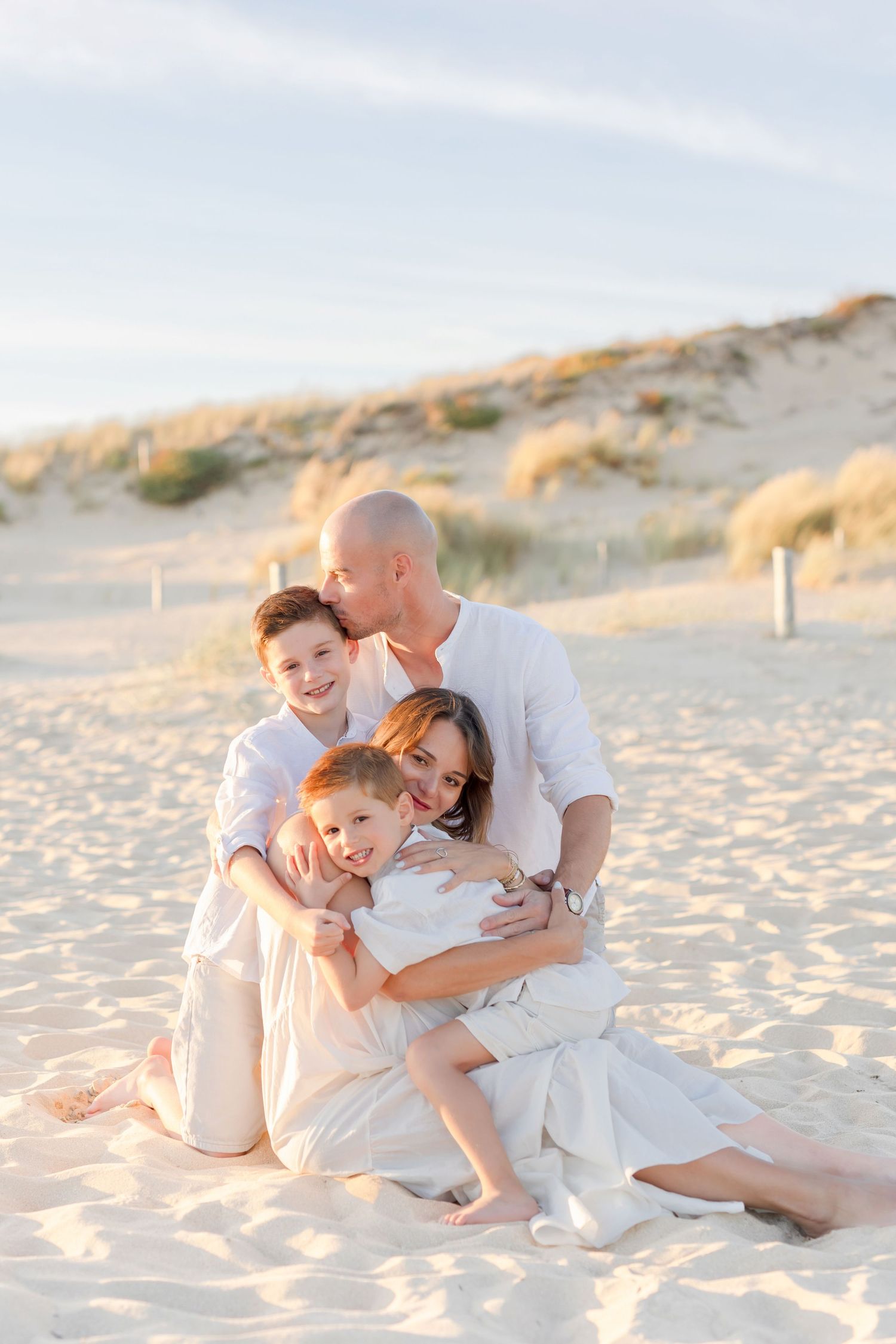 Family portrait on beach with sandy dunes in background during golden hour.