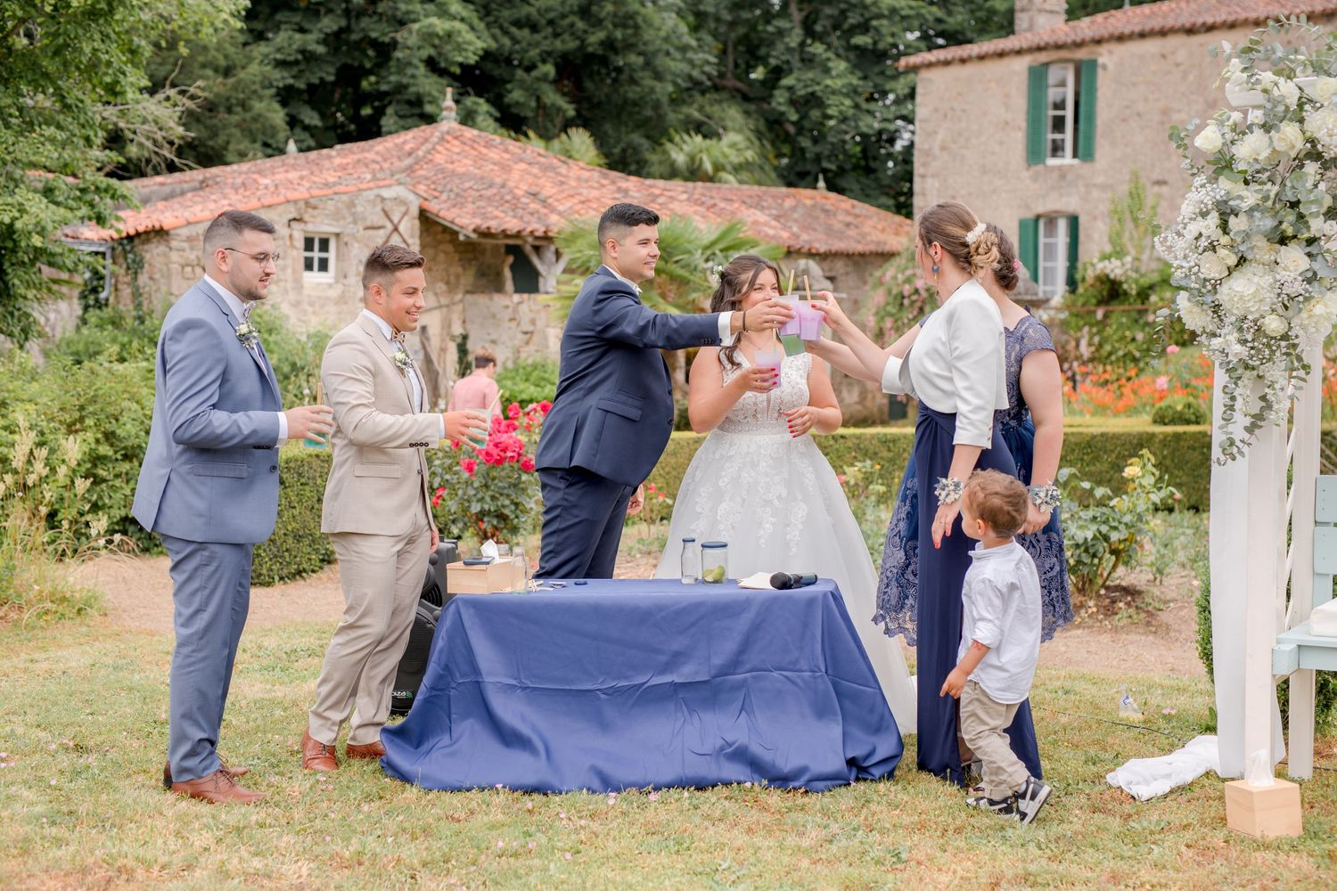 Group of wedding guests participate in a ritual around a blue table in a garden setting.
