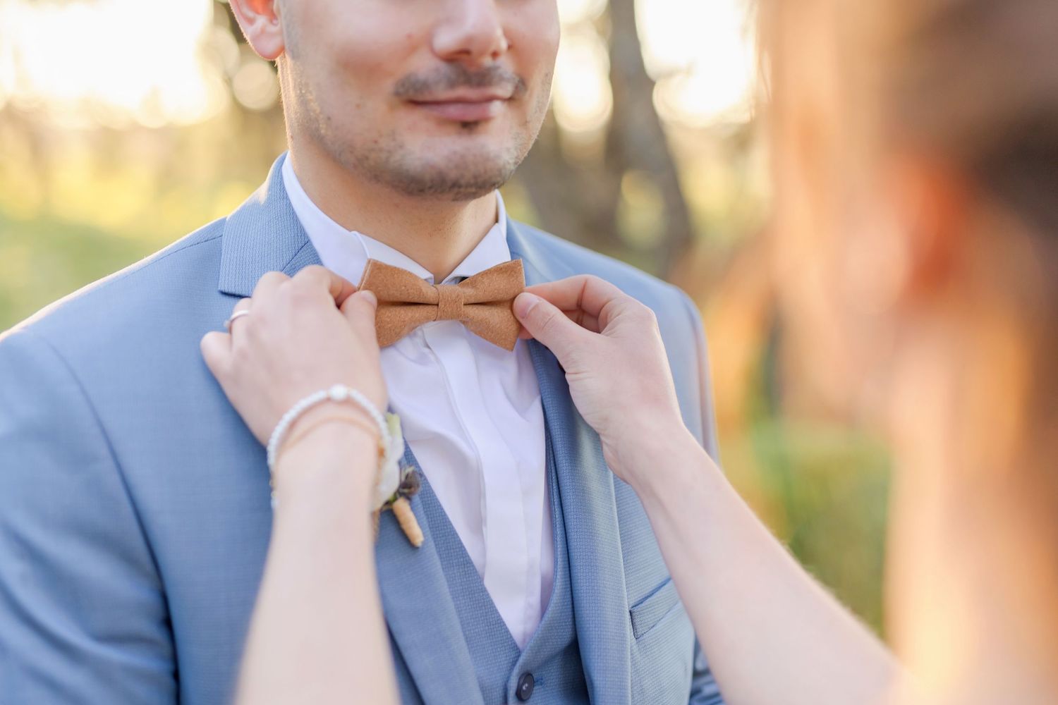 Person in blue suit having their peach colored bowtie adjusted outdoors.