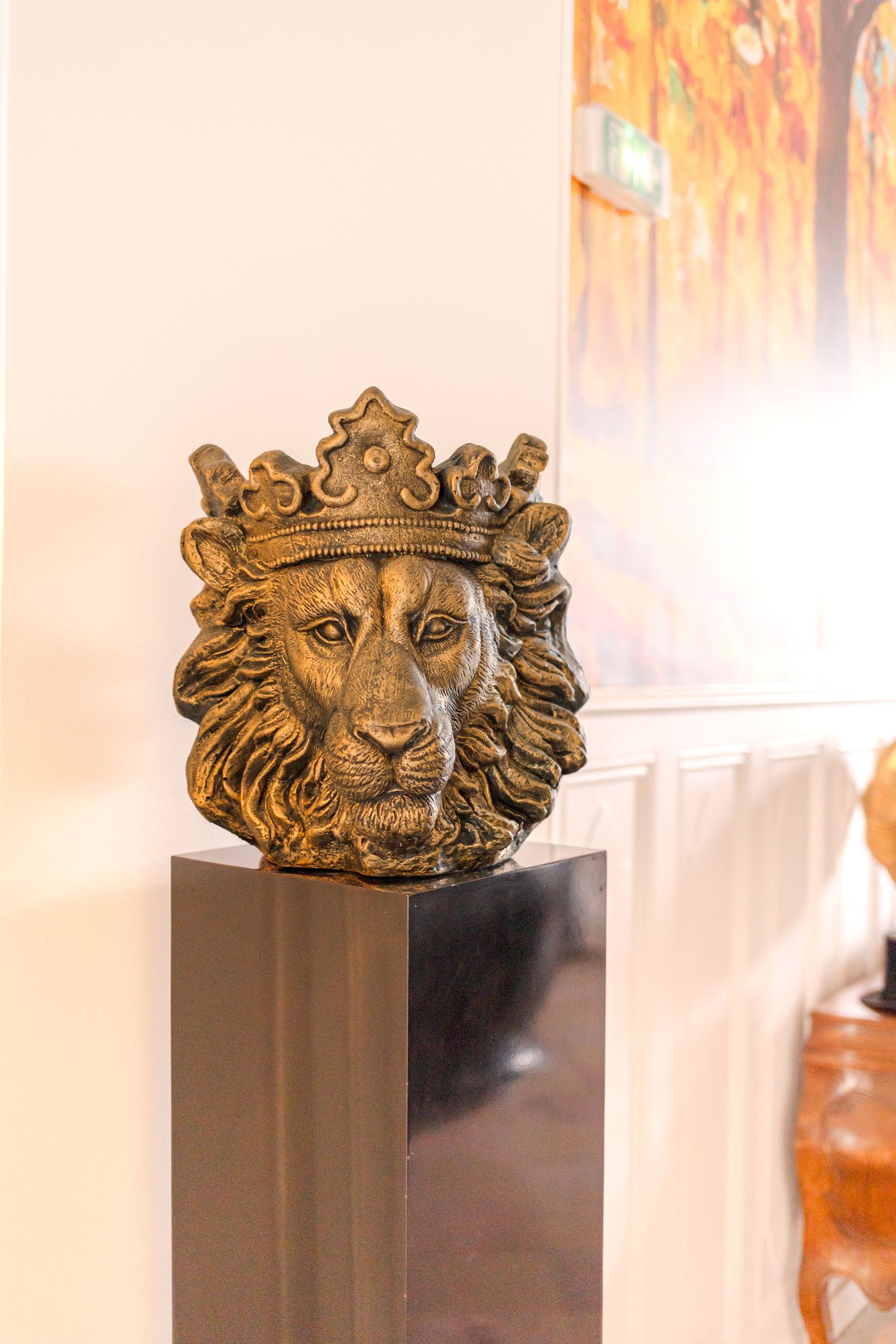 Decorative golden lion head sculpture with crown displayed on dark pedestal.