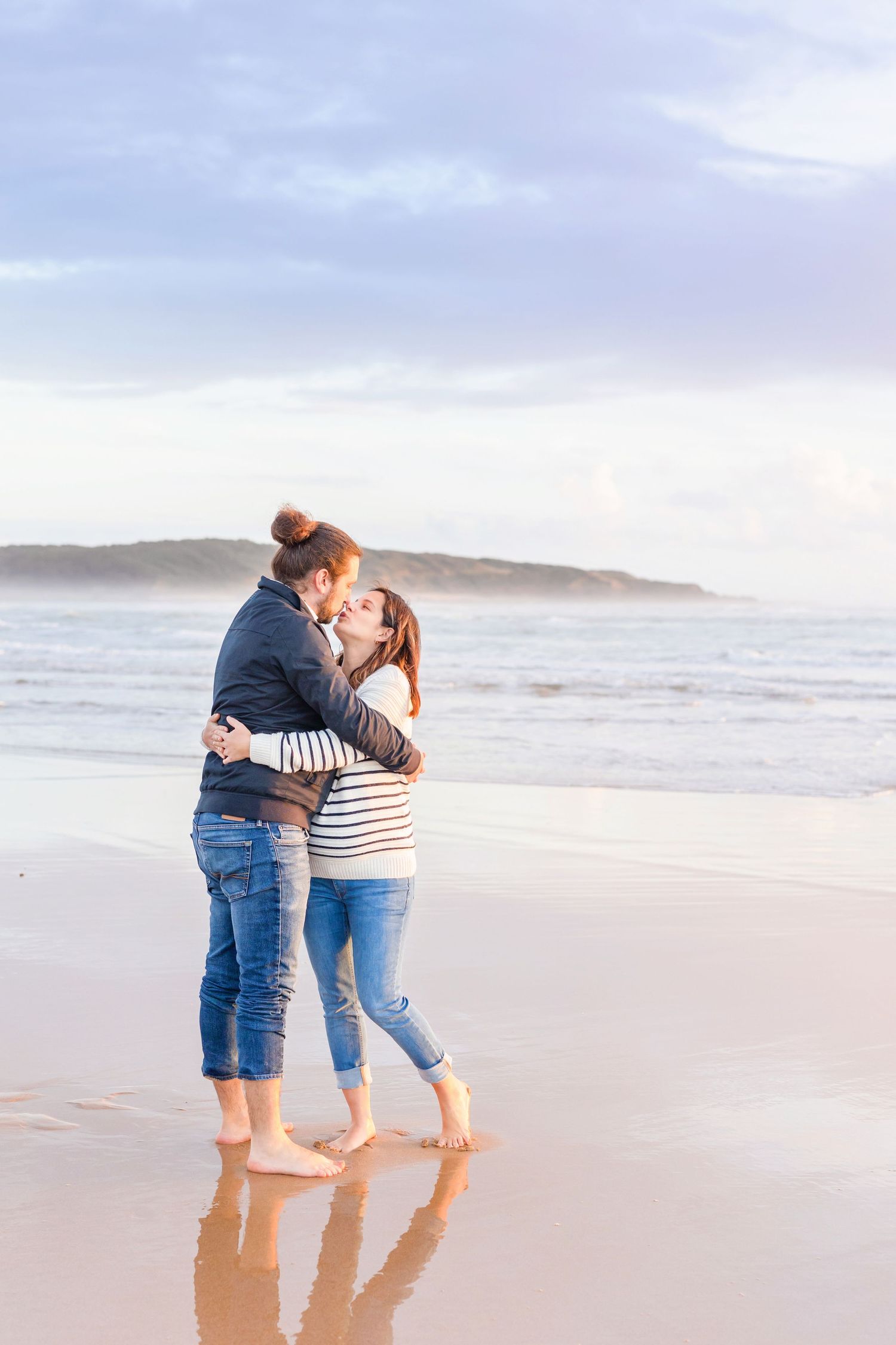 Couple embracing on beach during sunset maternity photoshoot.