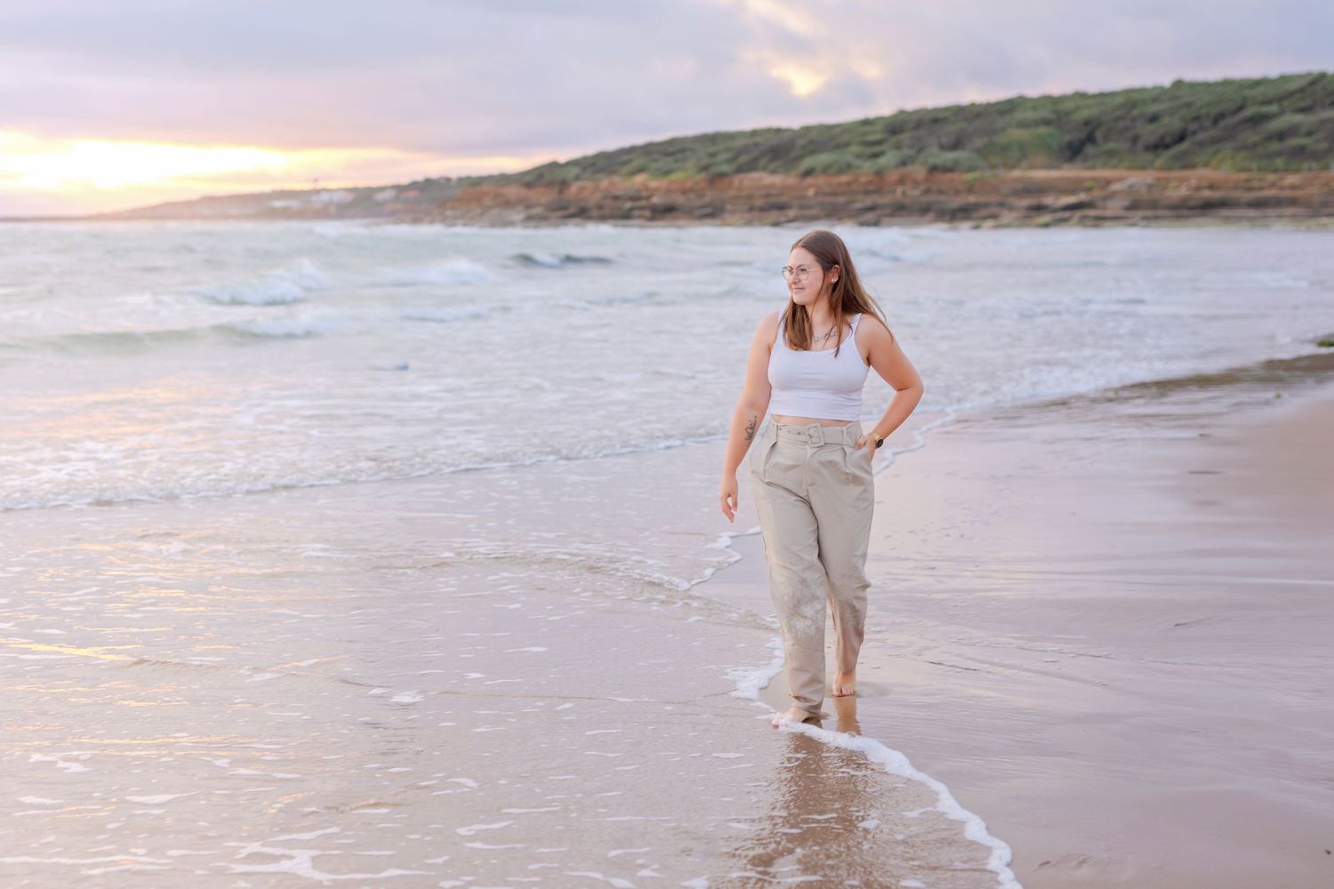 A person in casual attire walks along the shoreline during a peaceful beach sunset.