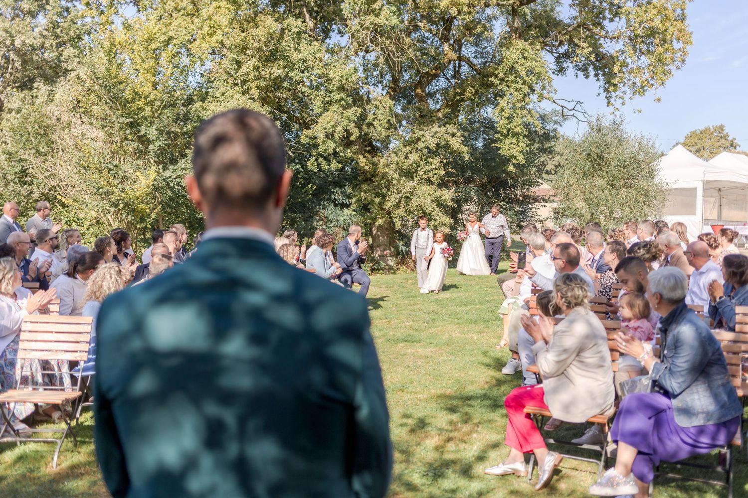View from behind speaker addressing seated wedding crowd outdoors.