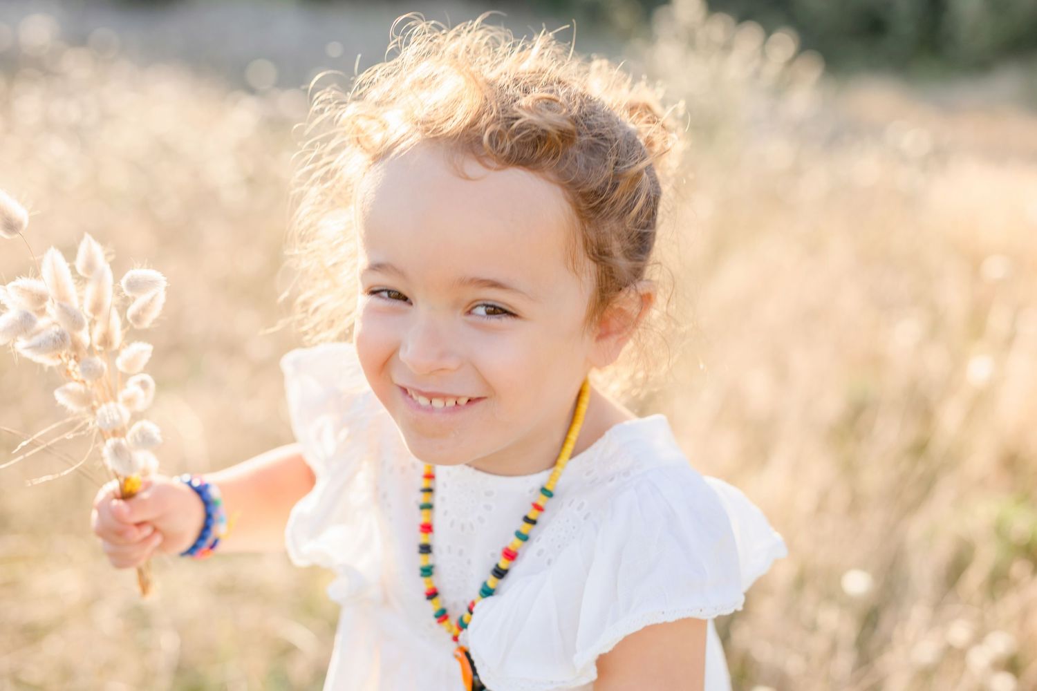 A bright smile shines while holding delicate dried flowers in a golden summer field.