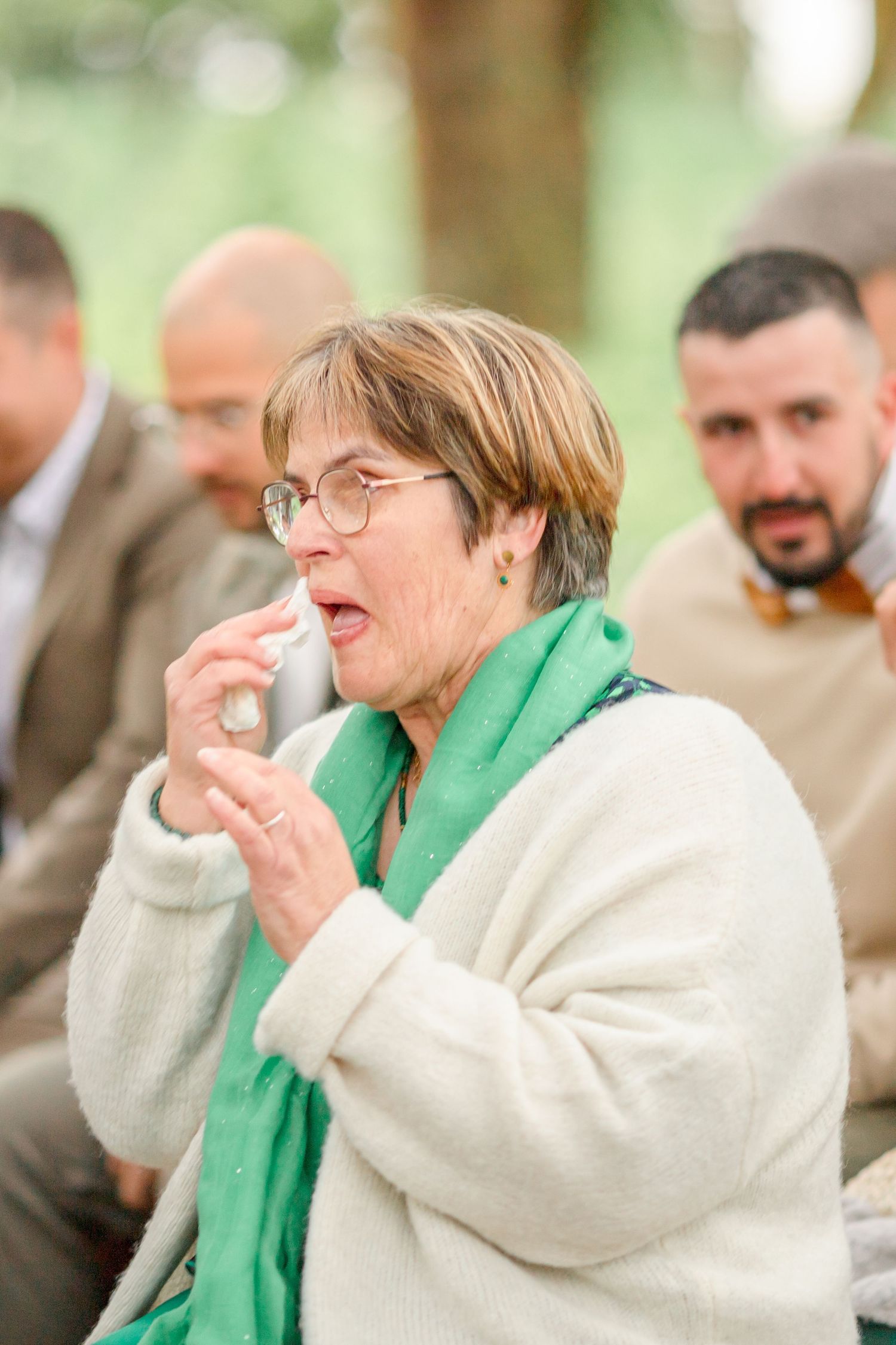 Guest in green scarf and white sweater shows emotional reaction during ceremony.