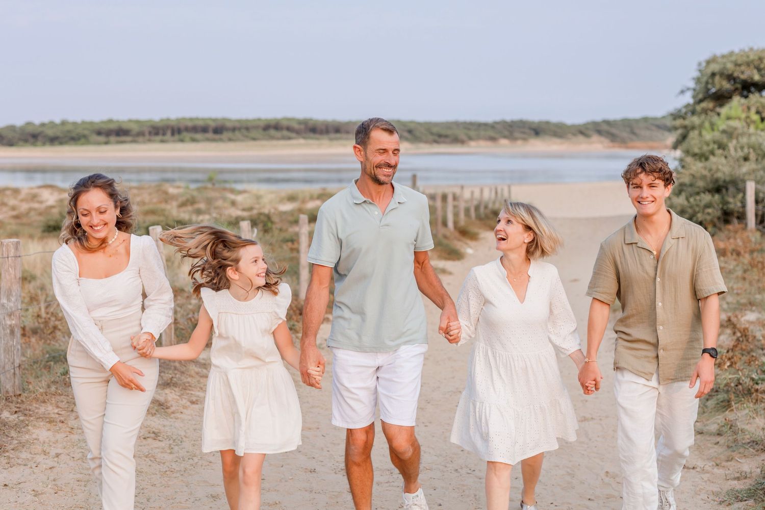 Family walking together on a sandy path at sunset wearing coordinated white and neutral colored outfits.