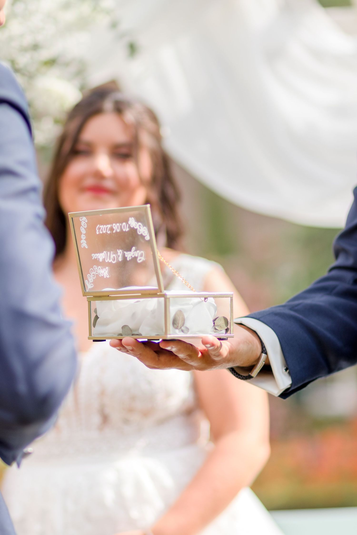 Clear glass ring box being presented during outdoor wedding ceremony.