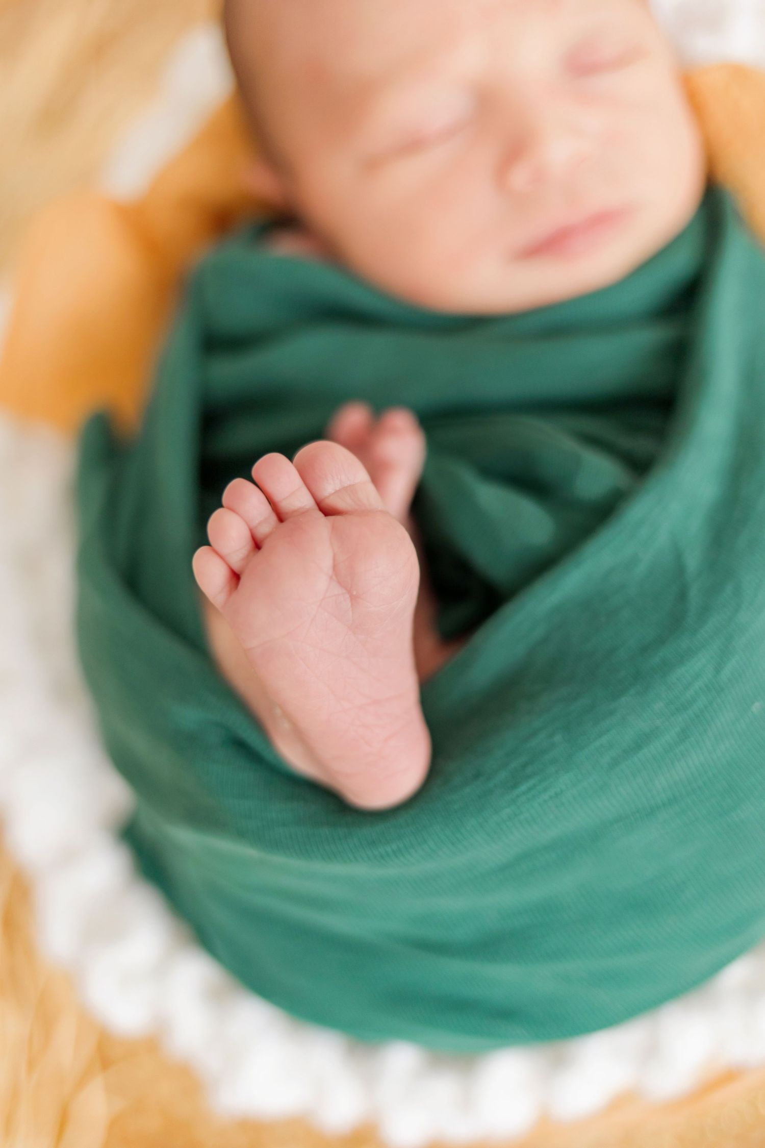 Close-up of tiny baby foot peeking out from emerald green swaddle wrap.