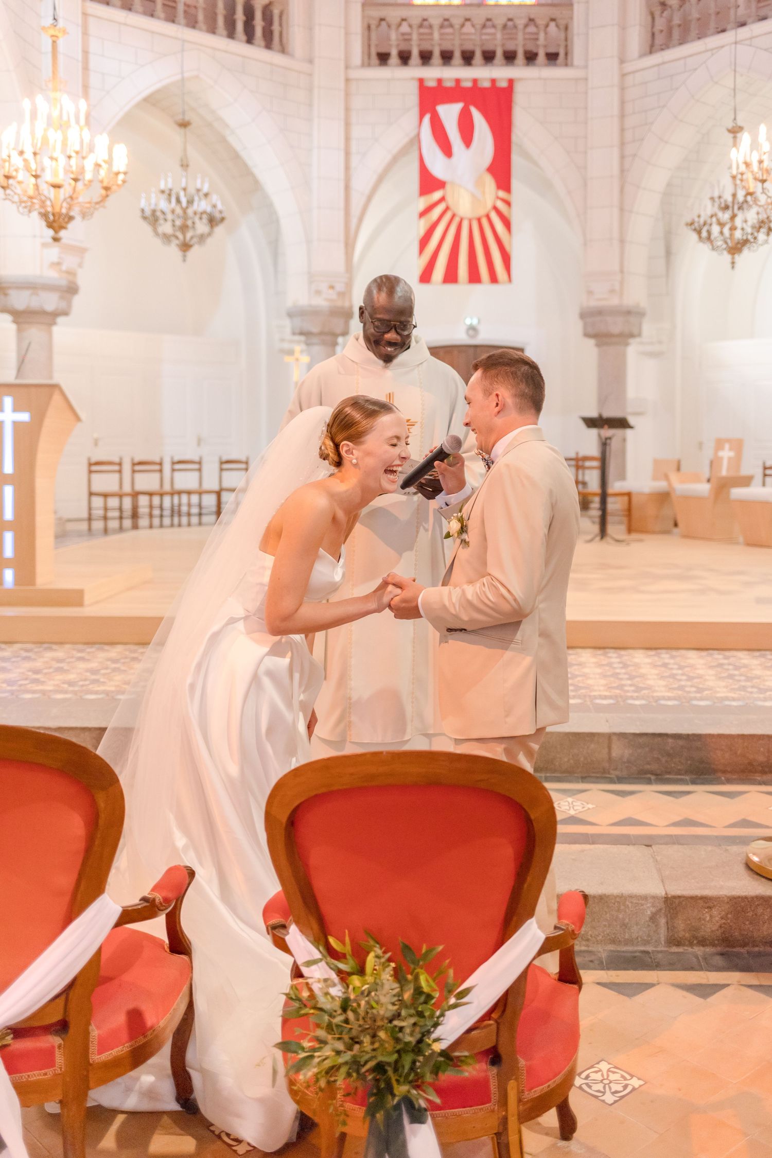 A joyful wedding moment captured in a beautiful church sanctuary with chandeliers and red banners.