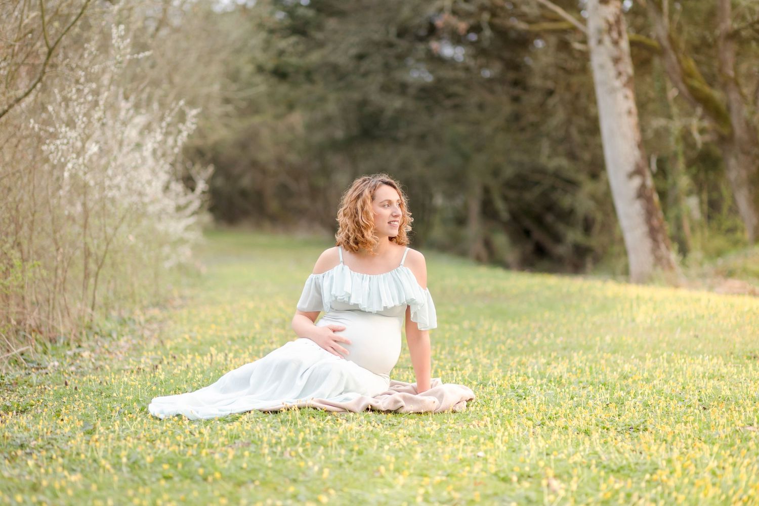 Maternity portrait of woman in pale blue dress sitting among spring wildflowers.