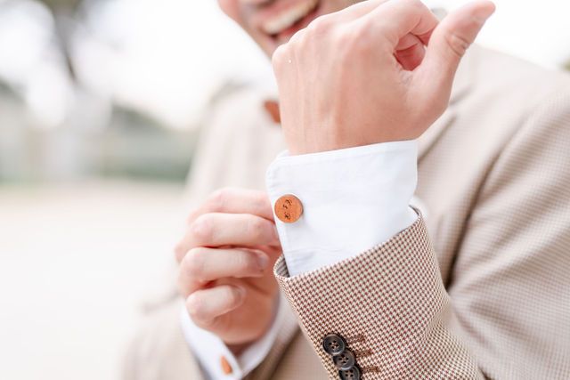 Detail shot of light tan suit sleeve with copper buttons and white cuff.
