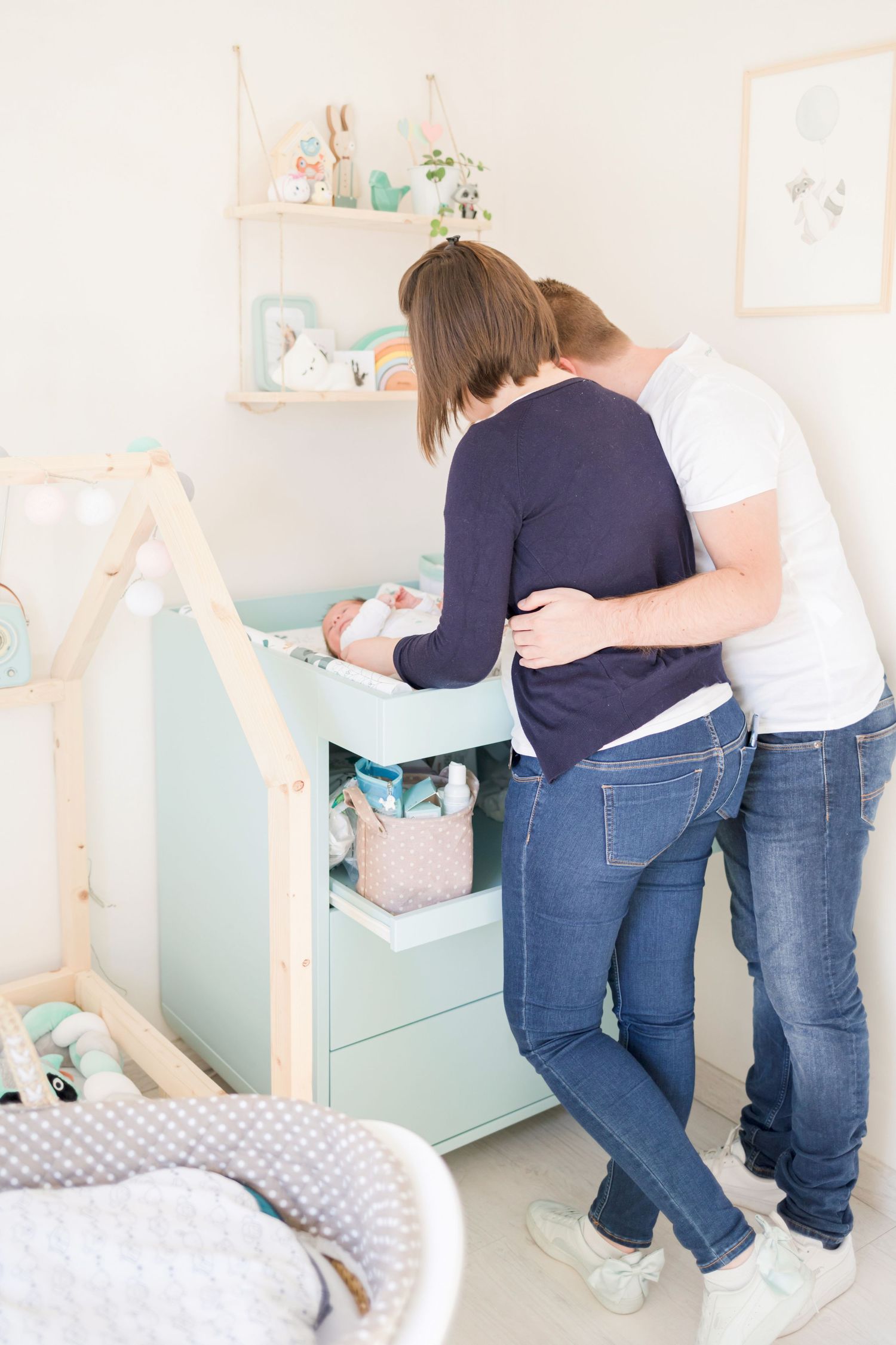 Family tending to baby at mint green changing table in modern minimalist nursery.