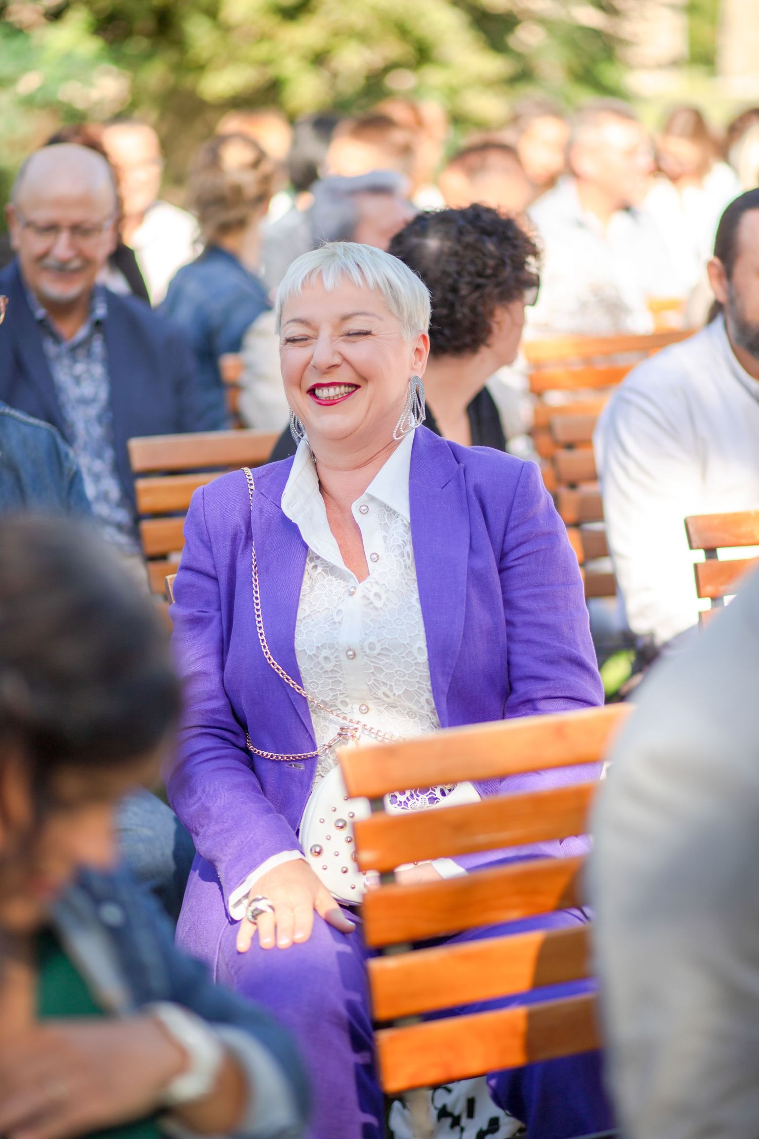 Wedding guest in bright purple blazer smiling during outdoor celebration.