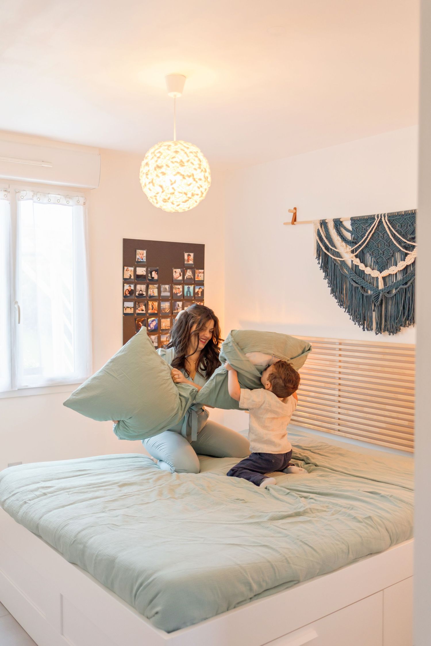 A playful pillow fight moment on a bed with mint green bedding under a modern spherical light fixture.