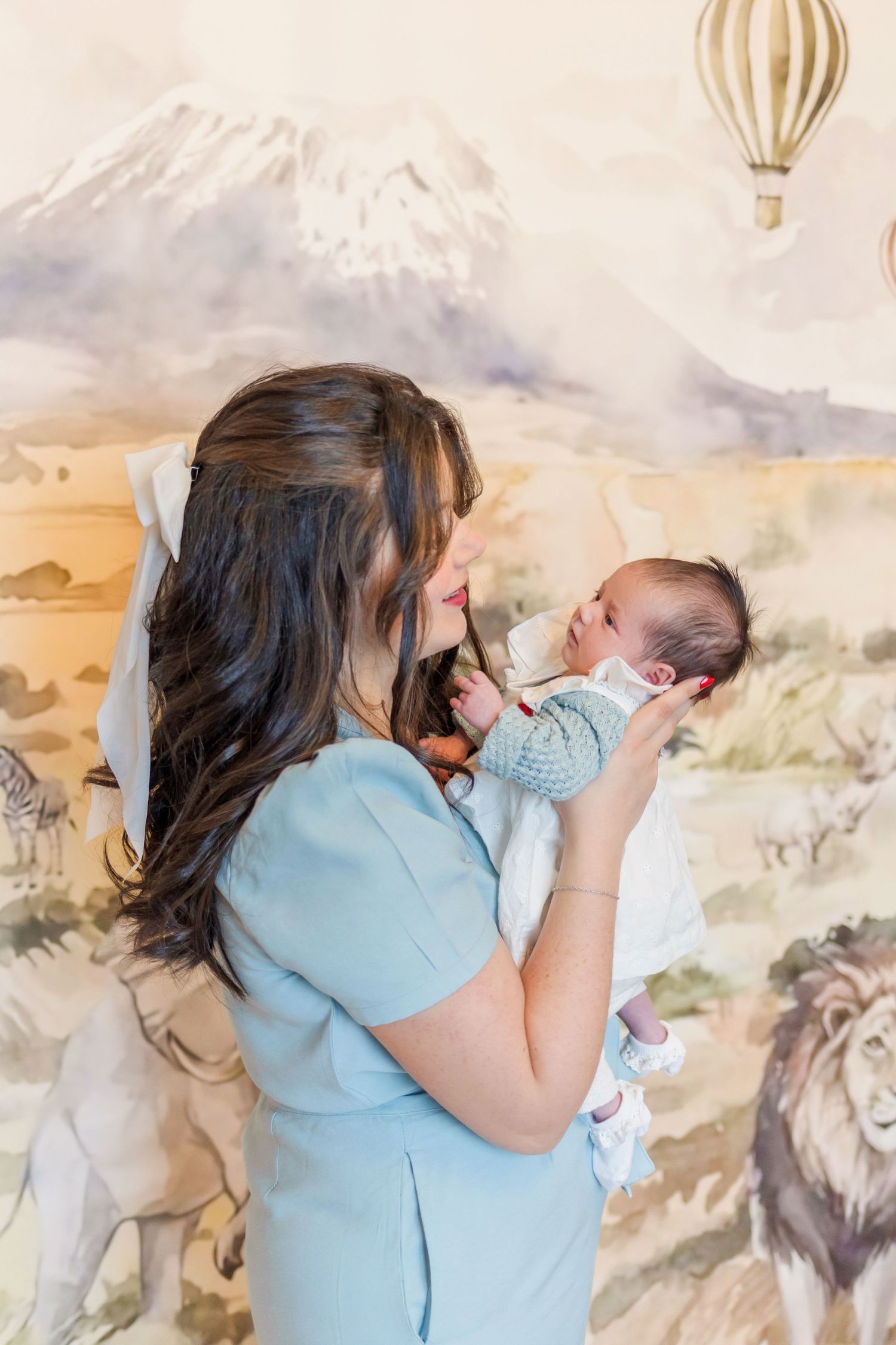 A tender nursery moment against a whimsical safari-themed wall mural with hot air balloons and mountains.