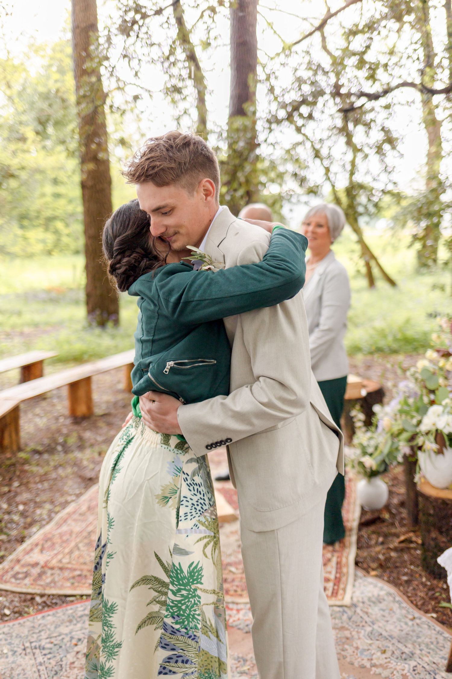Emotional embrace during outdoor woodland wedding ceremony with natural decor.