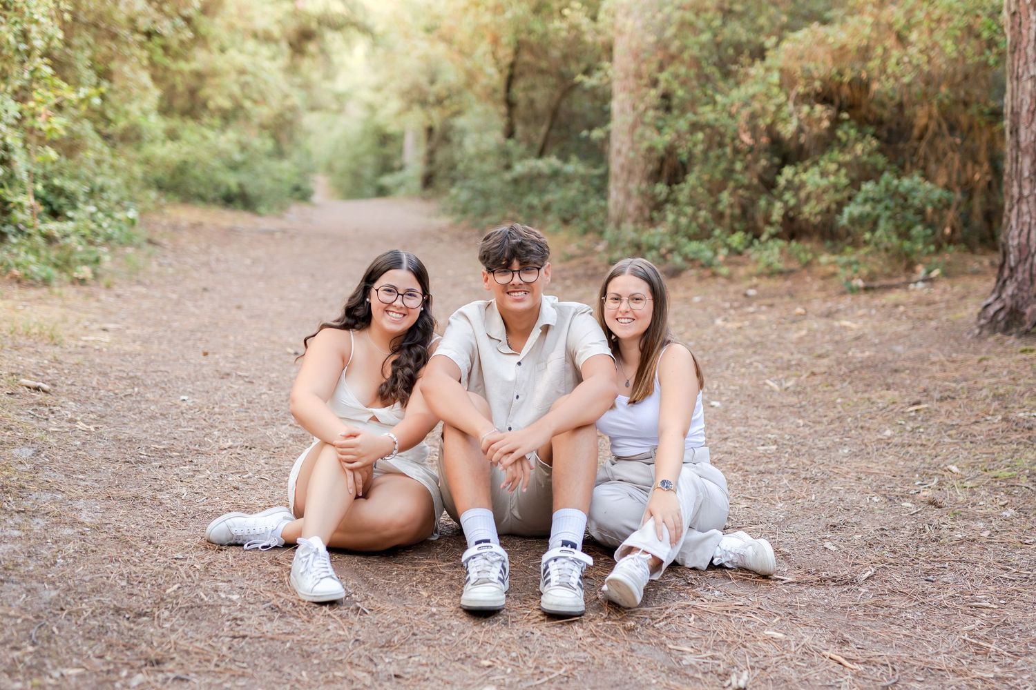 Three friends sitting together on a dirt path surrounded by lush greenery.