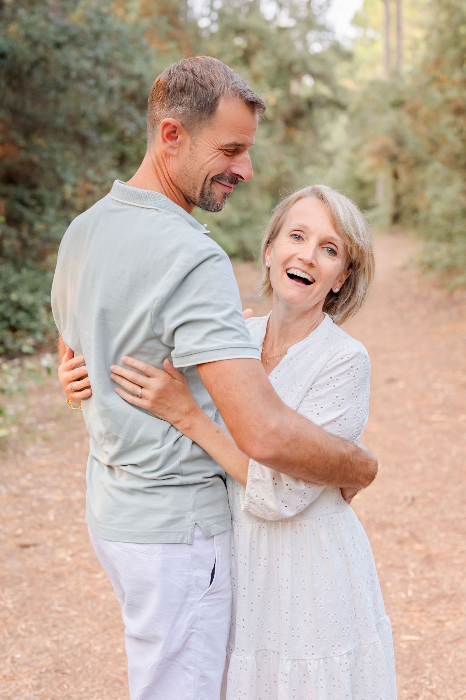 A couple in white and grey clothing laughs together during a photo session.