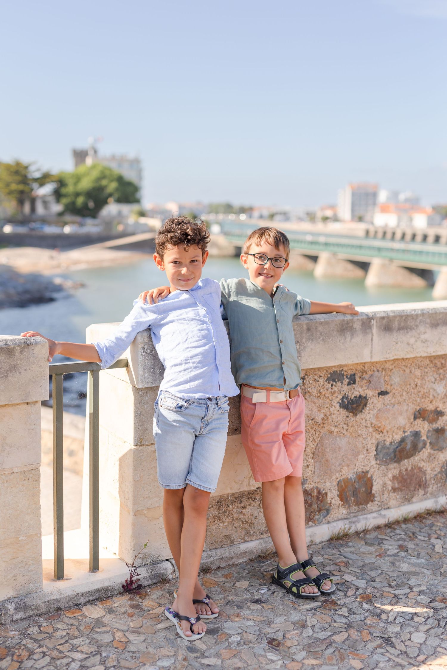 Two children looking over stone wall railing at waterfront view.