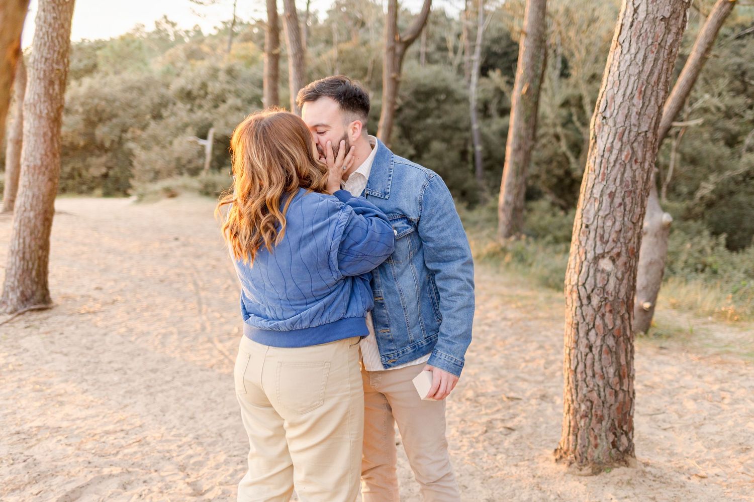 A romantic couple embraces while wearing matching denim jackets in a wooded setting.