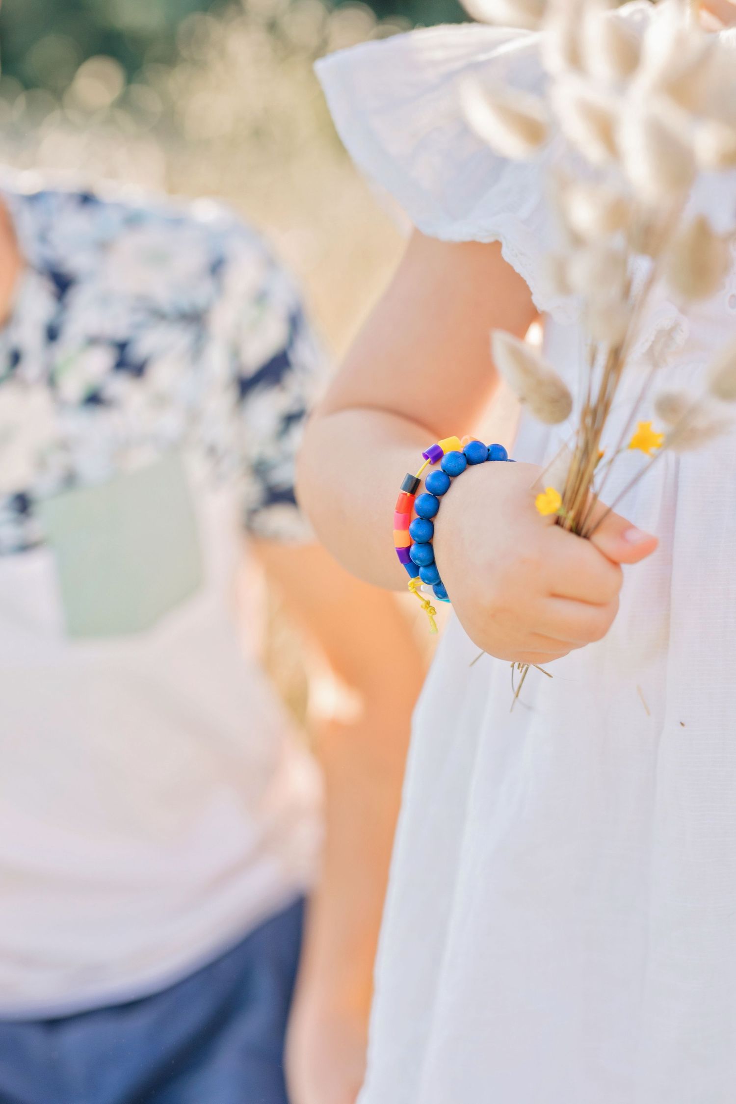 Close-up of hands holding dried flowers with blue and red beaded bracelet visible.