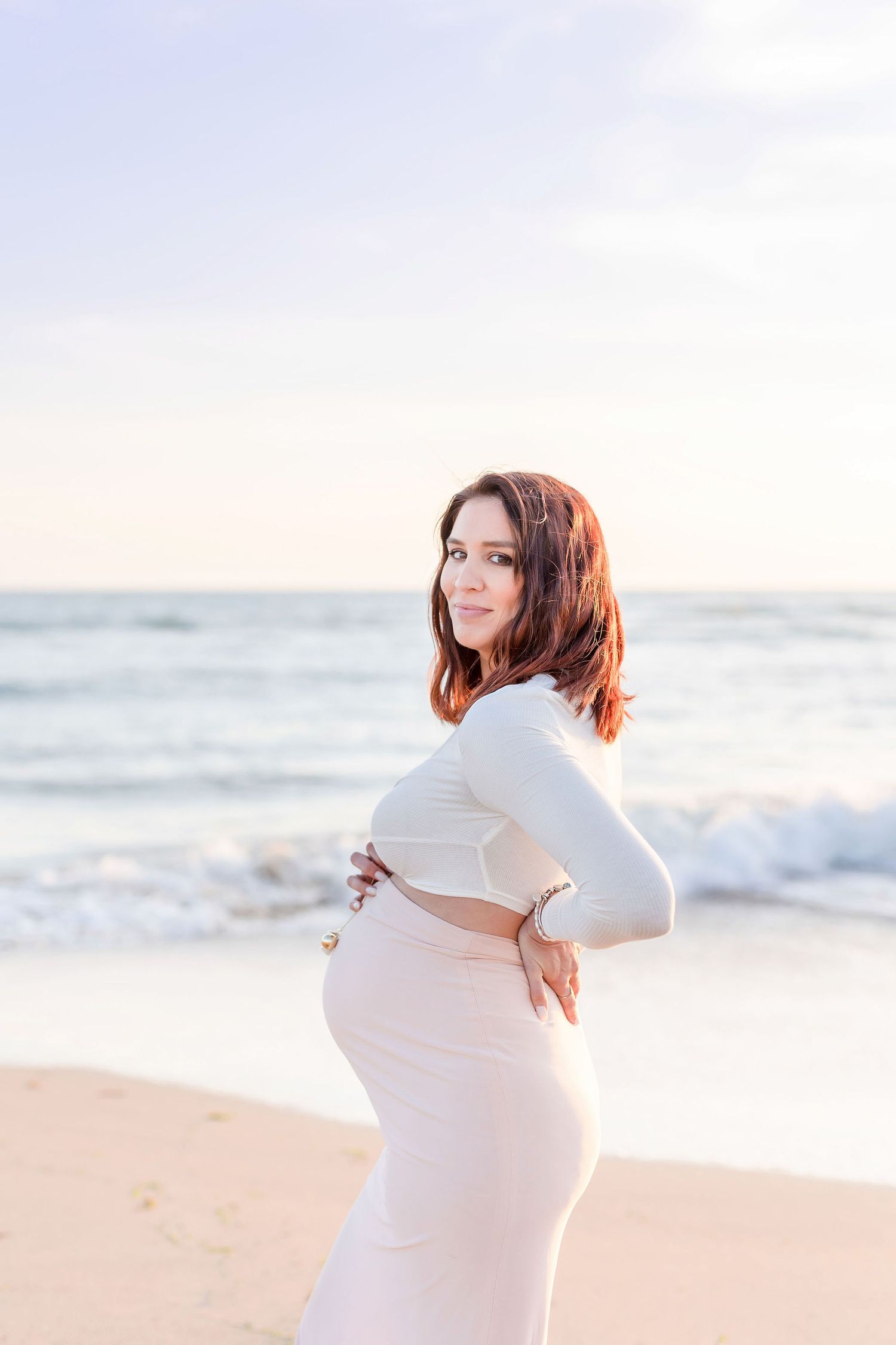 Beautiful maternity portraits captured against ocean waves and soft sunlight.
