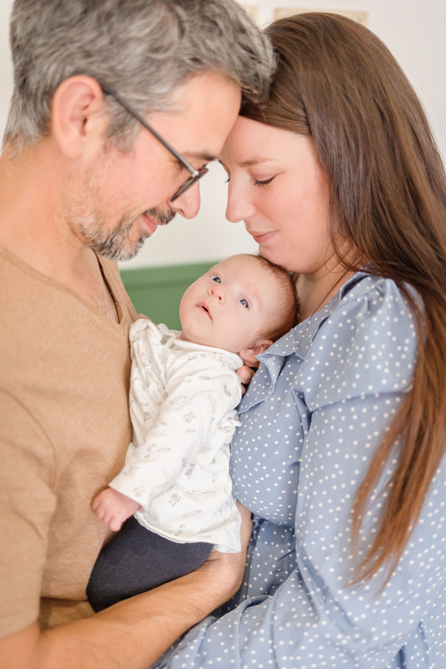Tender family moment captured against sage green nursery wall.