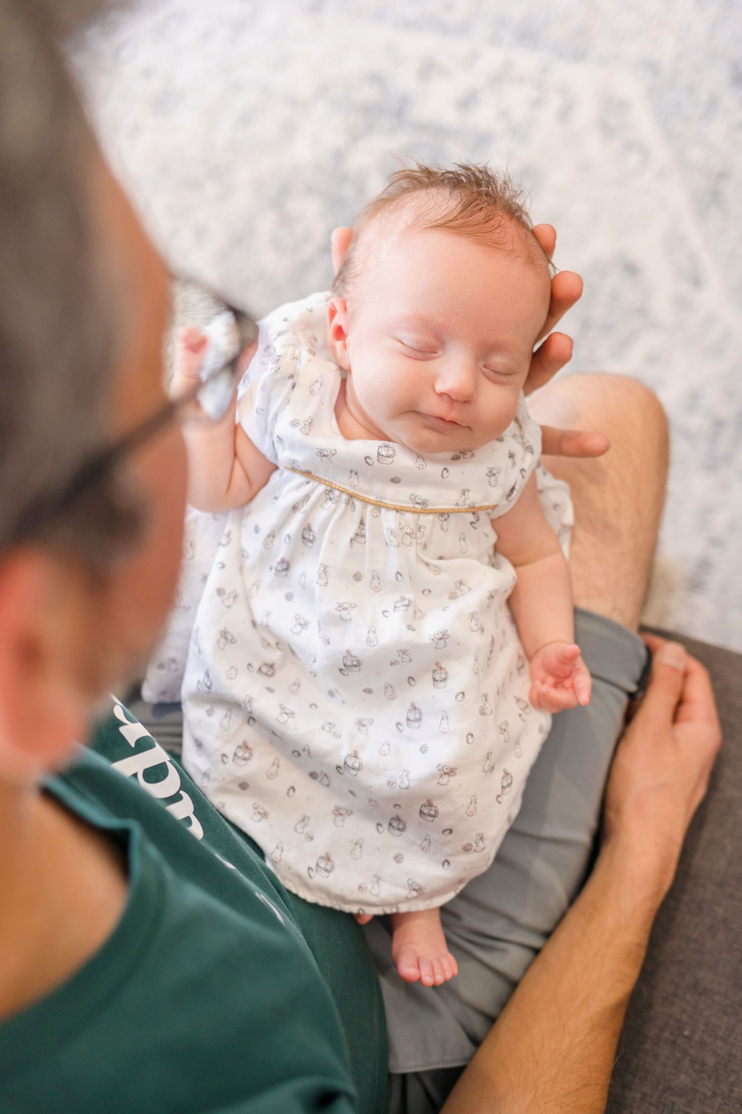 Peaceful sleeping baby in white dress resting on caregiver's lap.