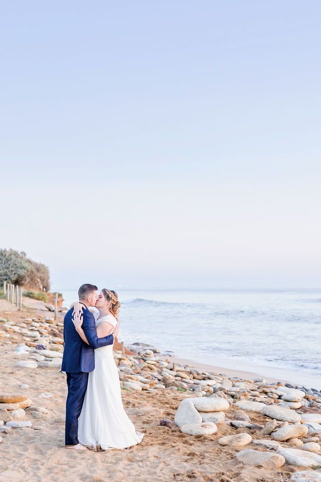 A romantic moment between newlyweds on a rocky beach at golden hour.