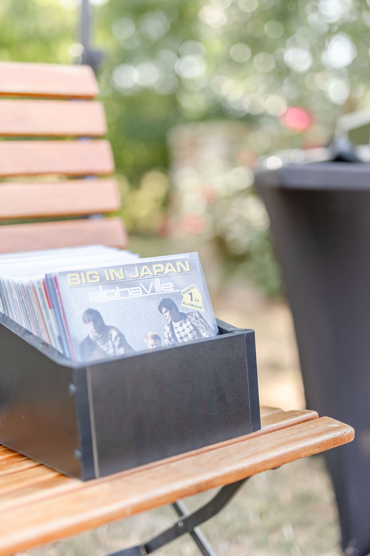 Black box filled with vinyl records on a wooden folding chair in an outdoor setting.