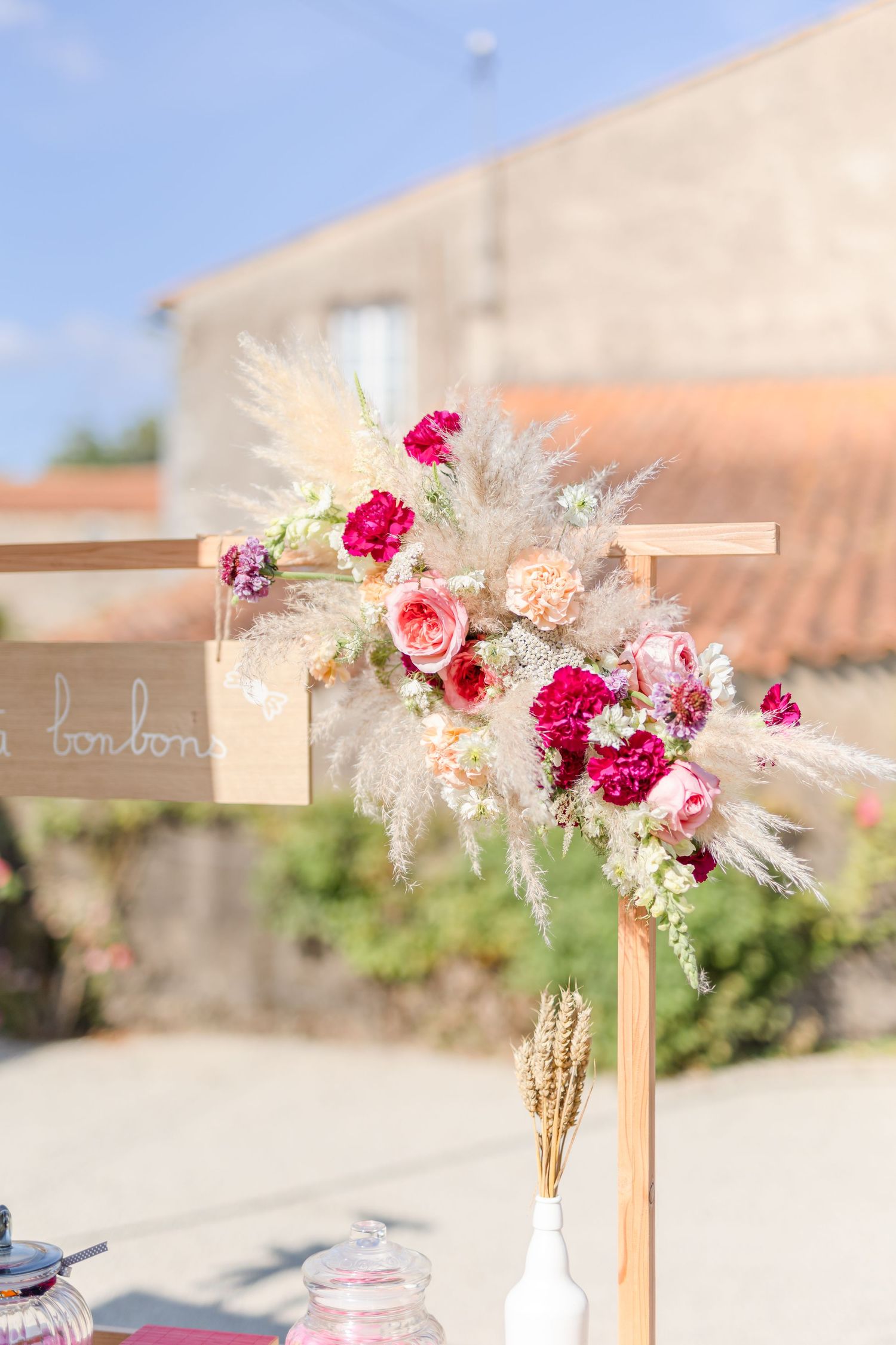 Elegant floral arrangement with pink roses and pampas grass on a wooden cross display.