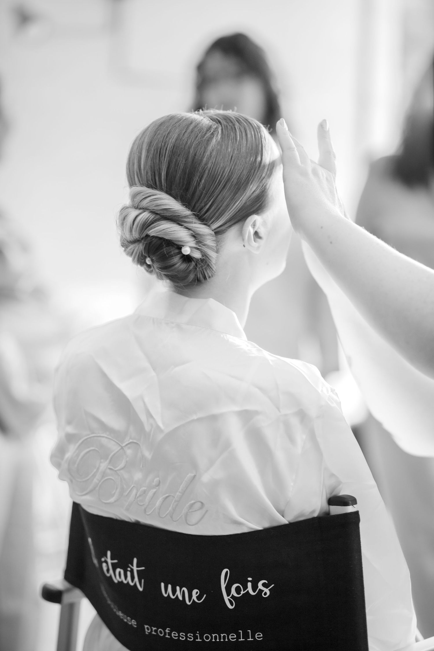 Elegant updo hairstyle being styled, with white robe showing French text.
