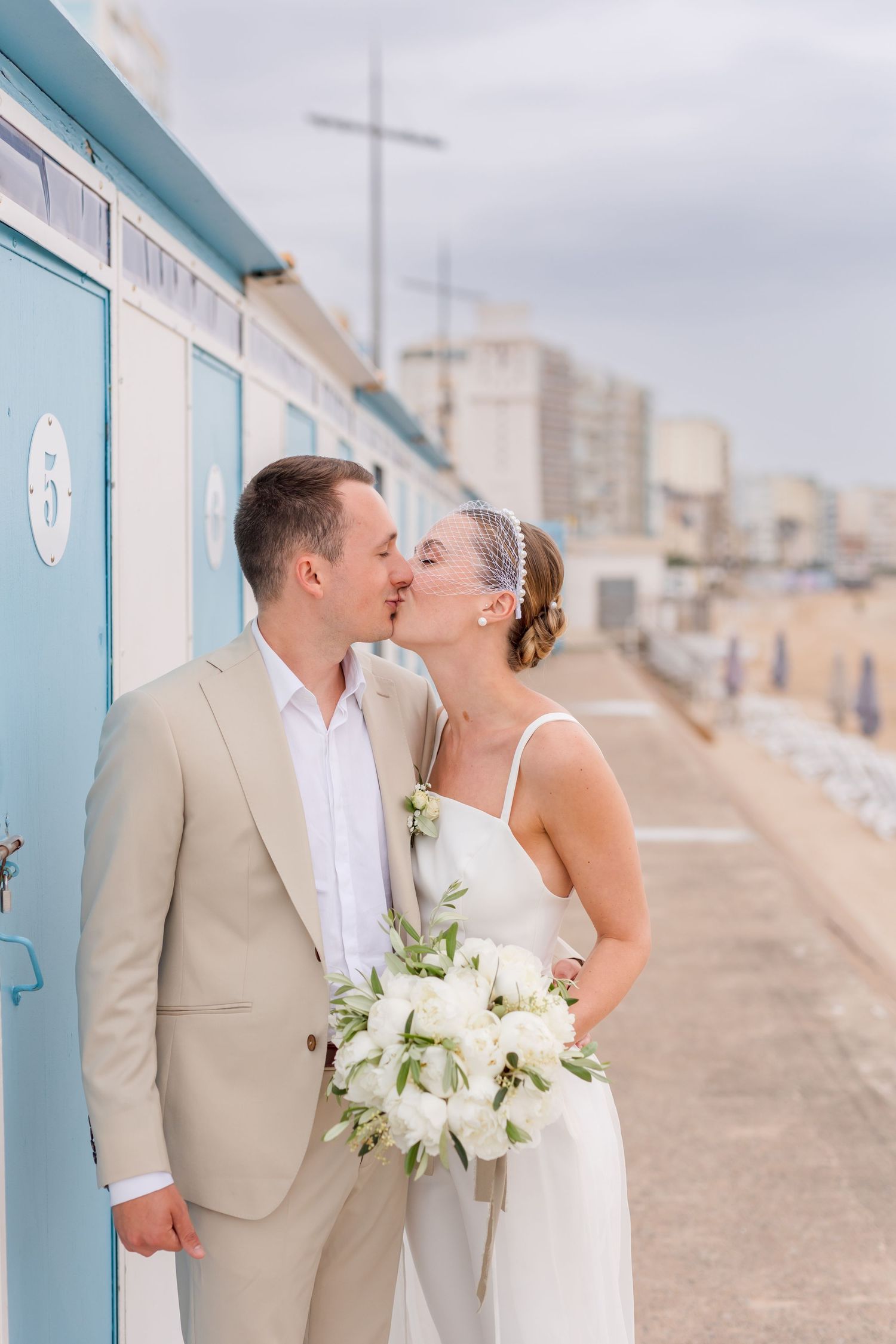 A tender moment shared against blue beach huts with a seaside backdrop.