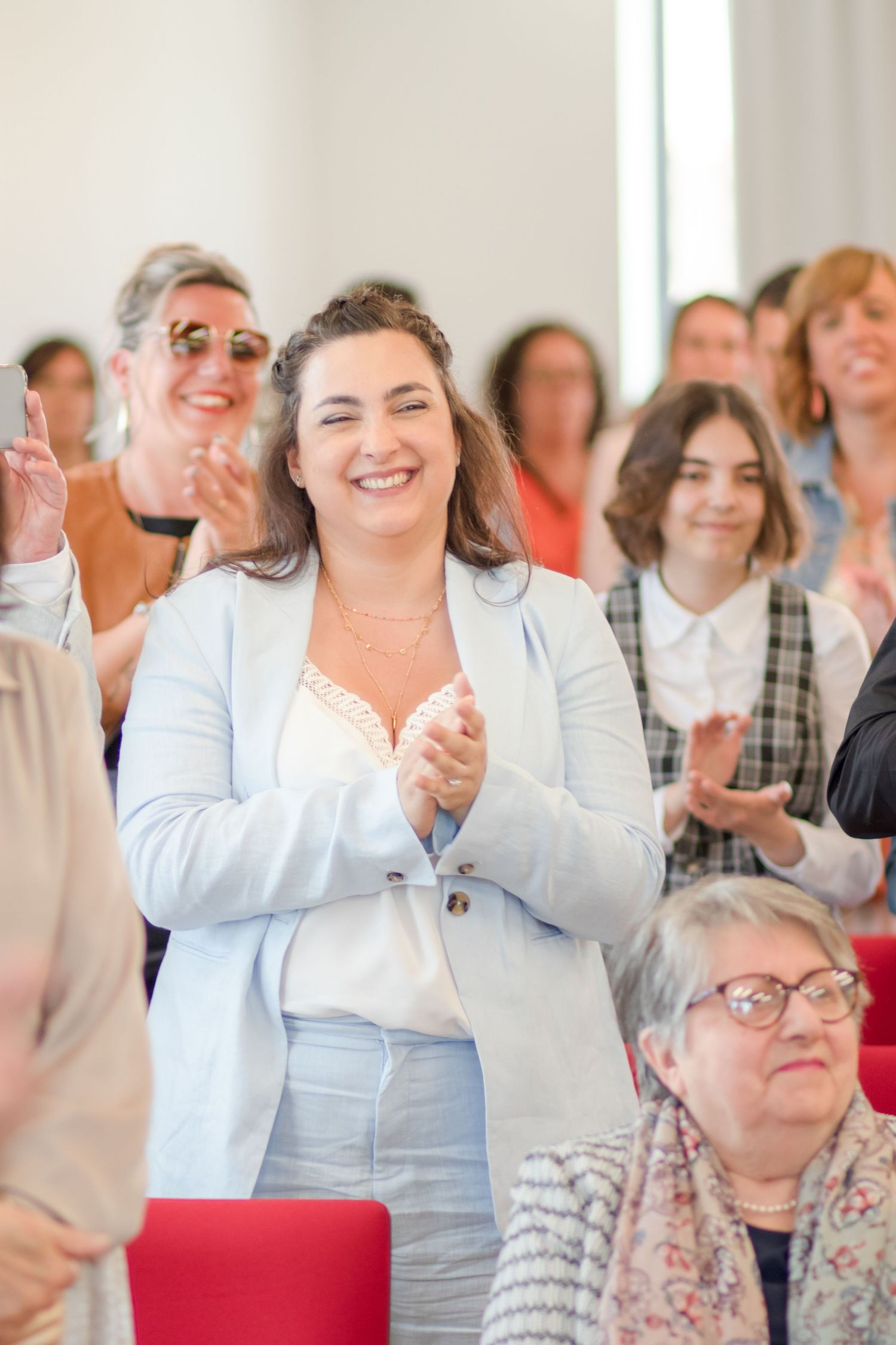 Wedding guests in light colored attire applaud during celebration.