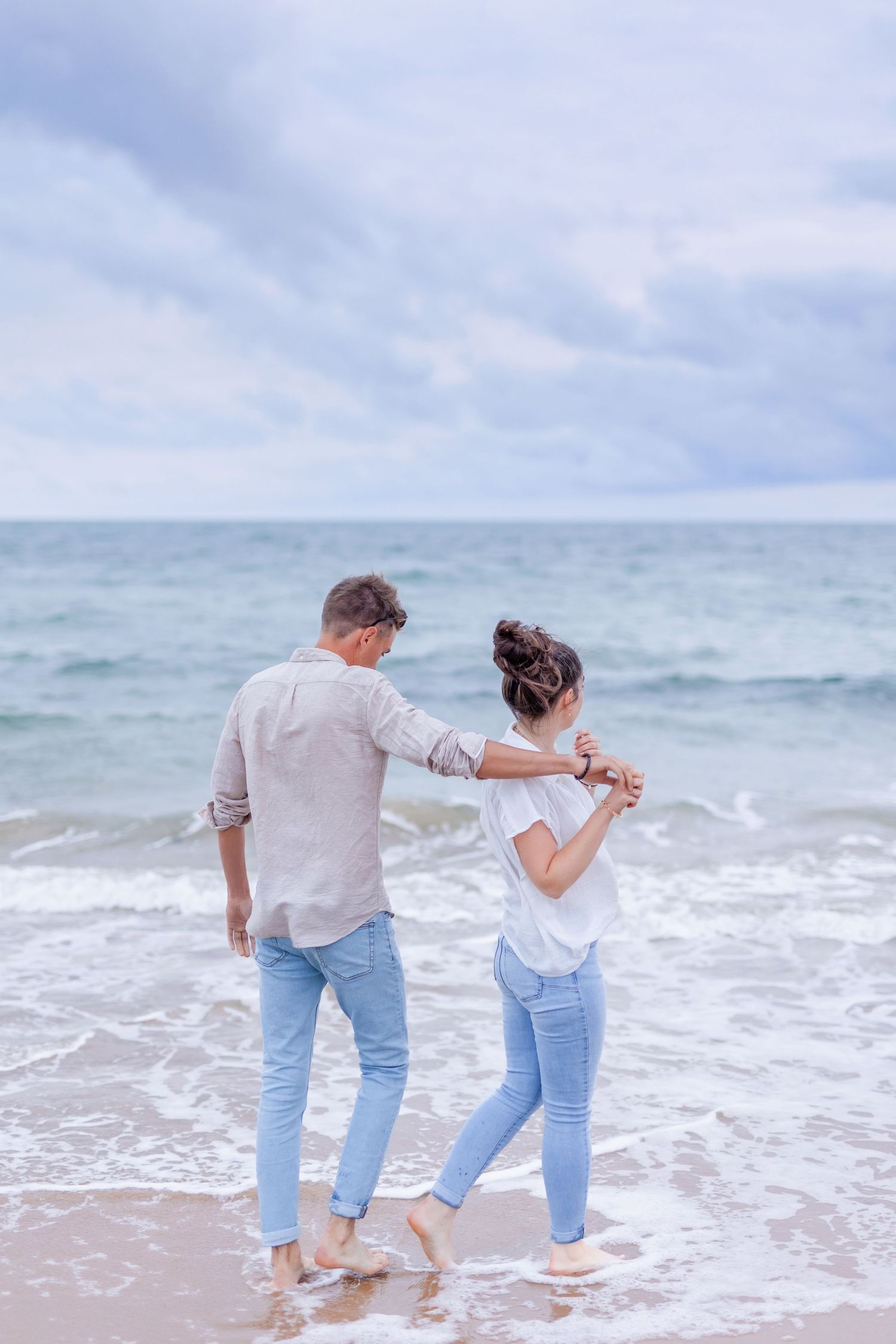 Couple holding hands while standing in ocean waves at beach.