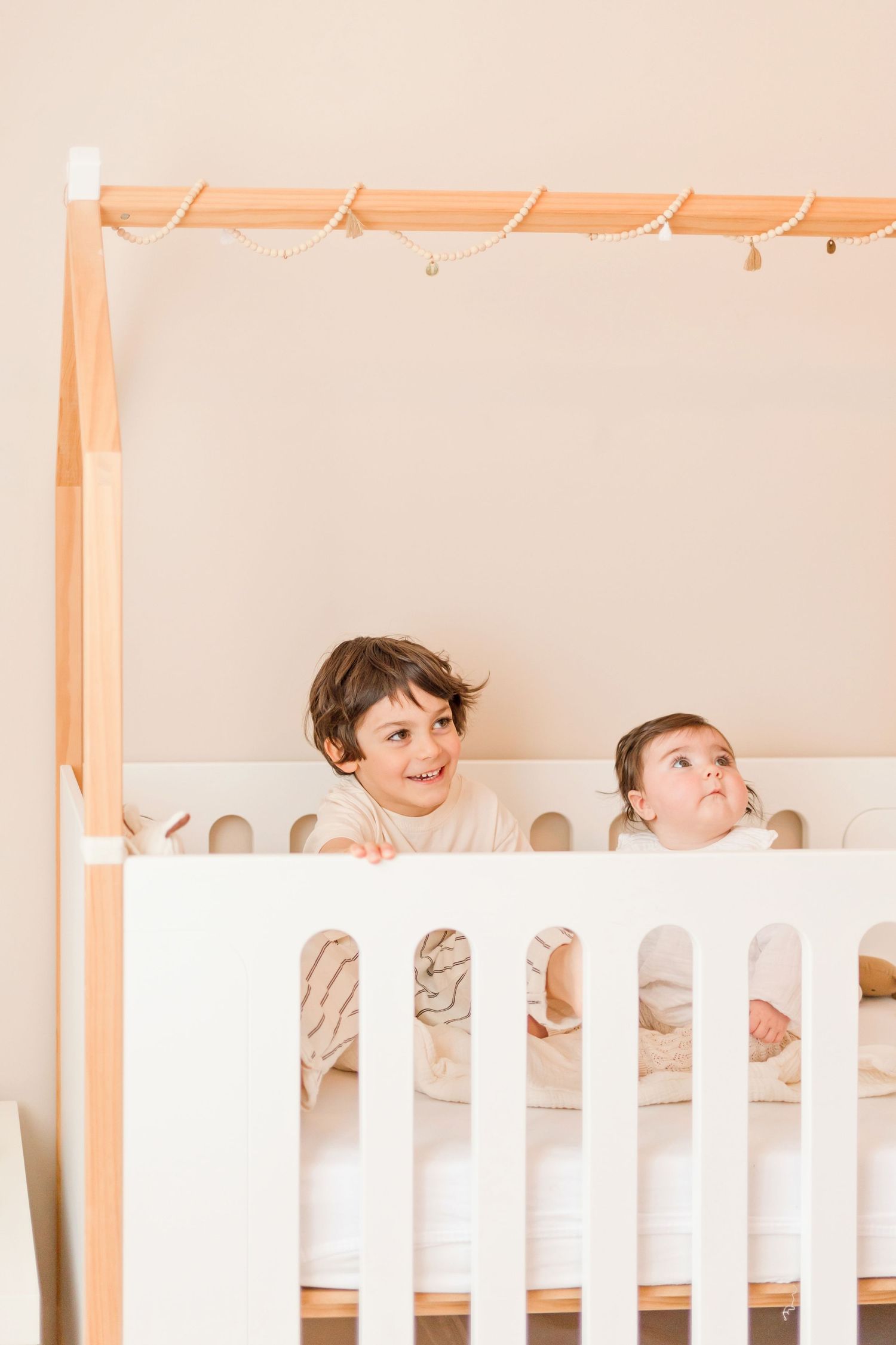 Children peek playfully through wooden crib slats in a bright nursery.