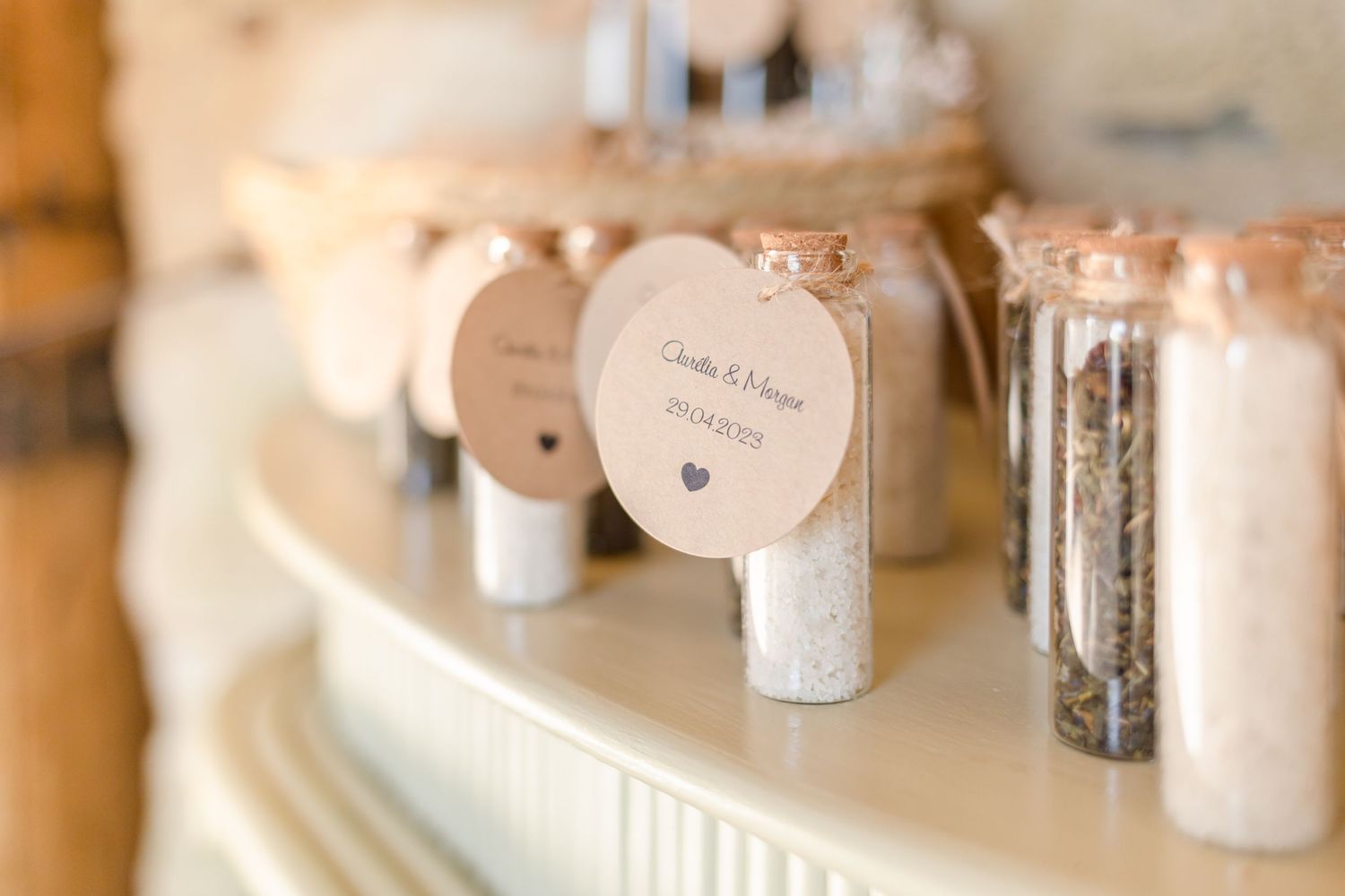 Wedding favor bottles with cork stoppers displayed on white shelf.